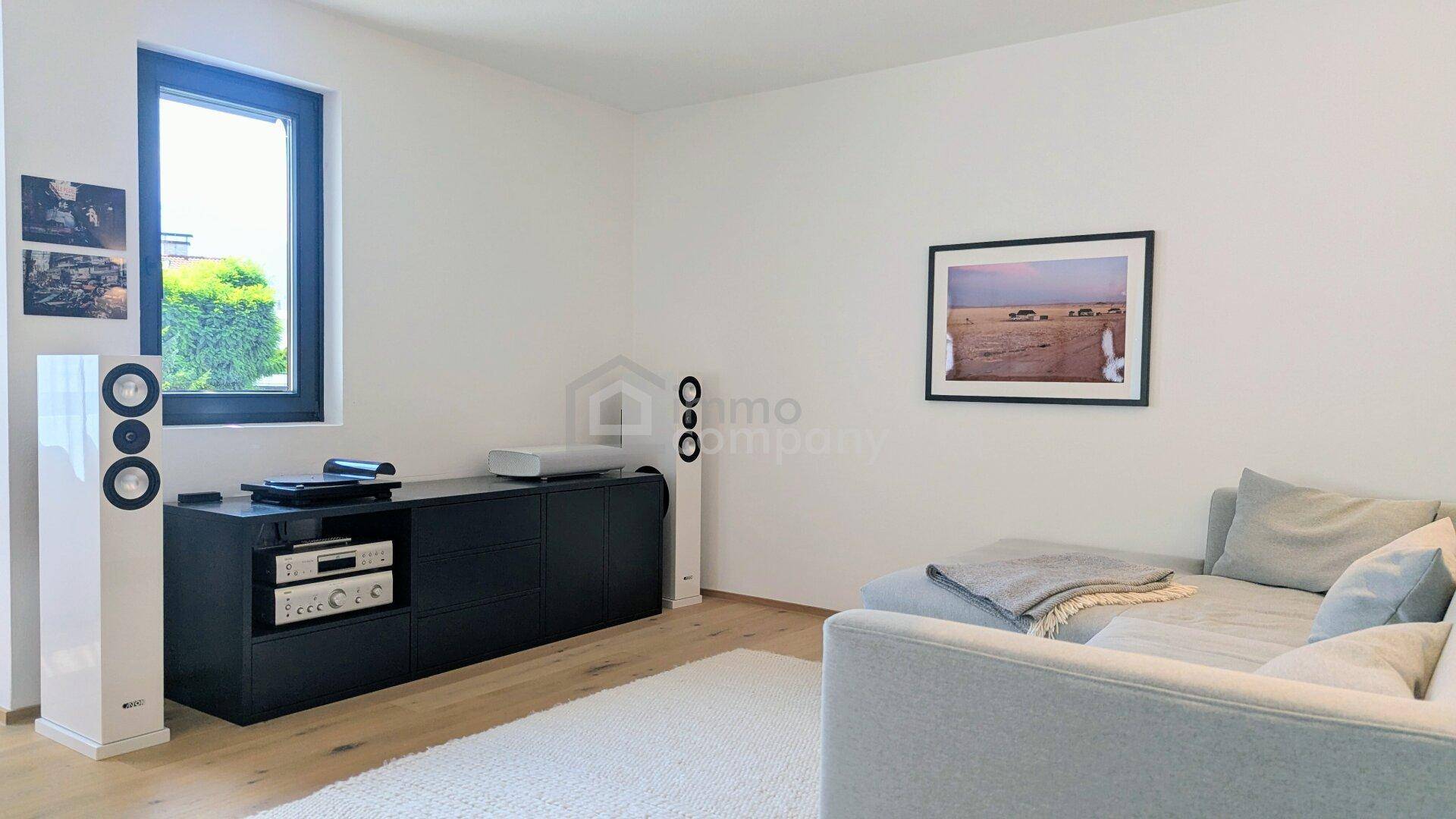 Gemütliche Wohnzimmerecke mit Sofa, Medienschrank und Fensterblick ins Grüne, ideal zum Entspannen.