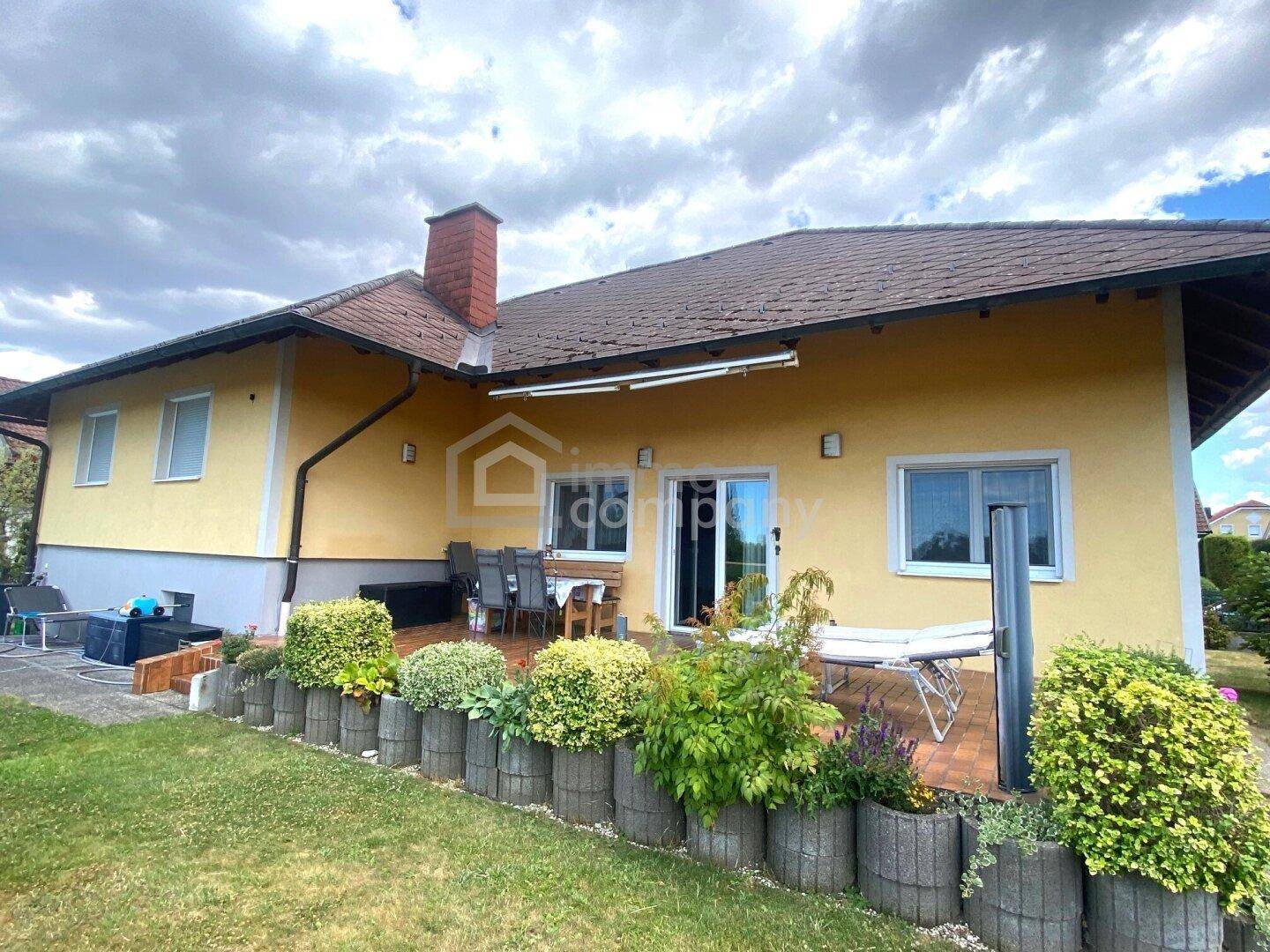 Rückseite des Hauses mit gelber Fassade, großer Terrasse und gepflegtem Gartenbereich.