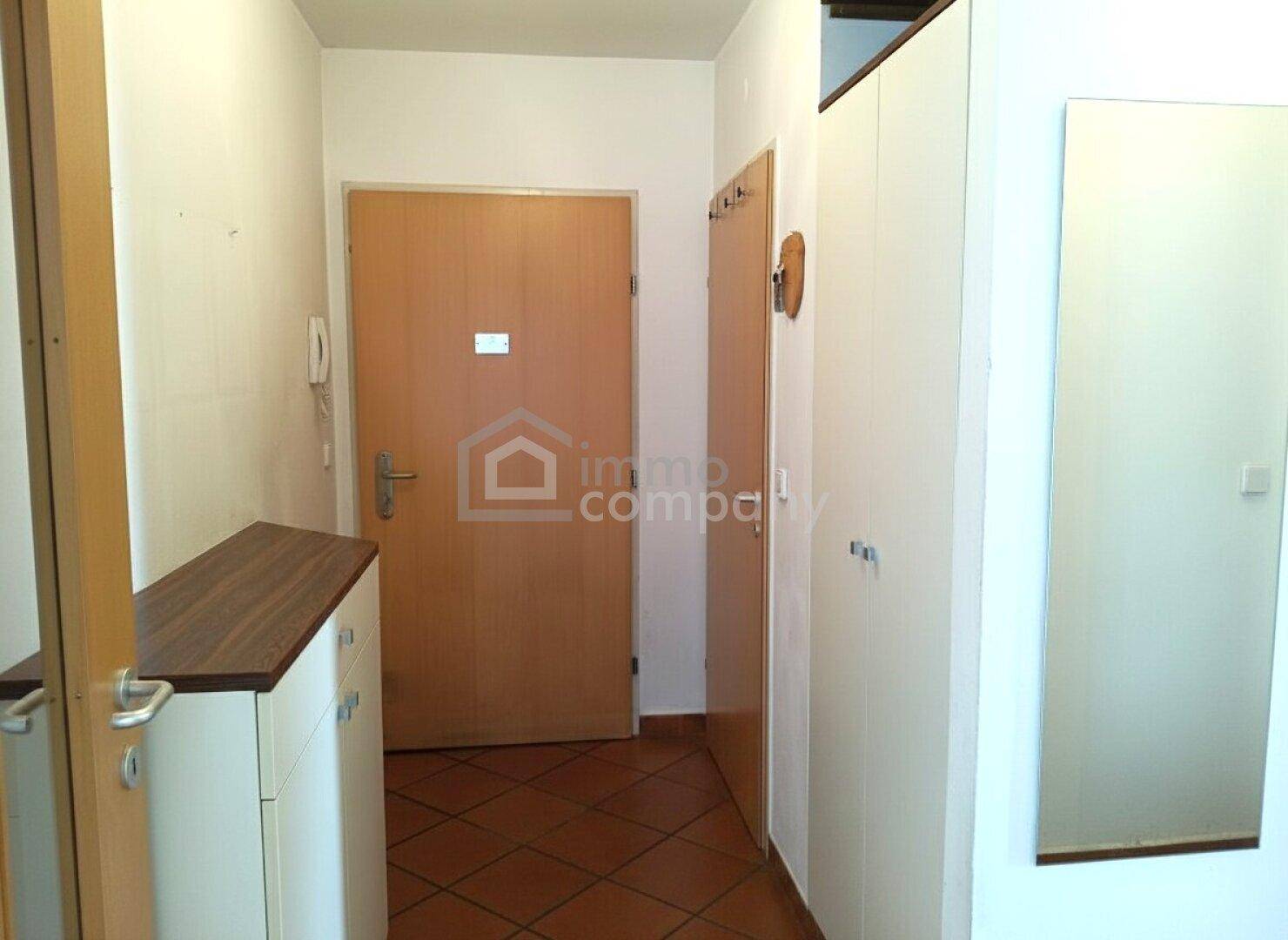 Heller Eingangsbereich mit Terrakotta-Fliesenboden, Garderobe und großem Wandspiegel.