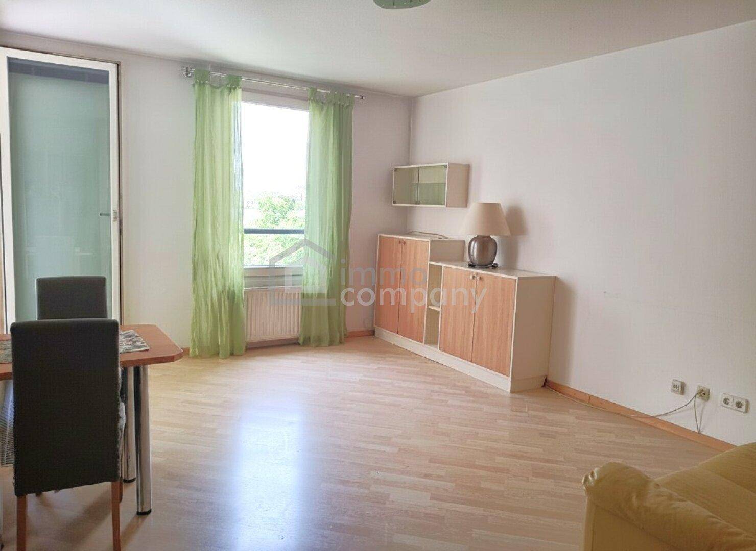Heller Wohn- und Essbereich mit hellem Holzboden, Fenster und Zugang zu einem Balkon oder Terrasse.