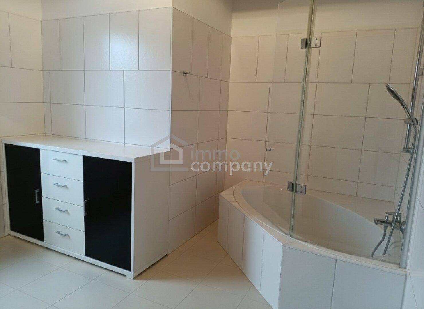Helles Badezimmer mit weißen Fliesen, einer Eckbadewanne und einem modernen Waschtischunterschrank.