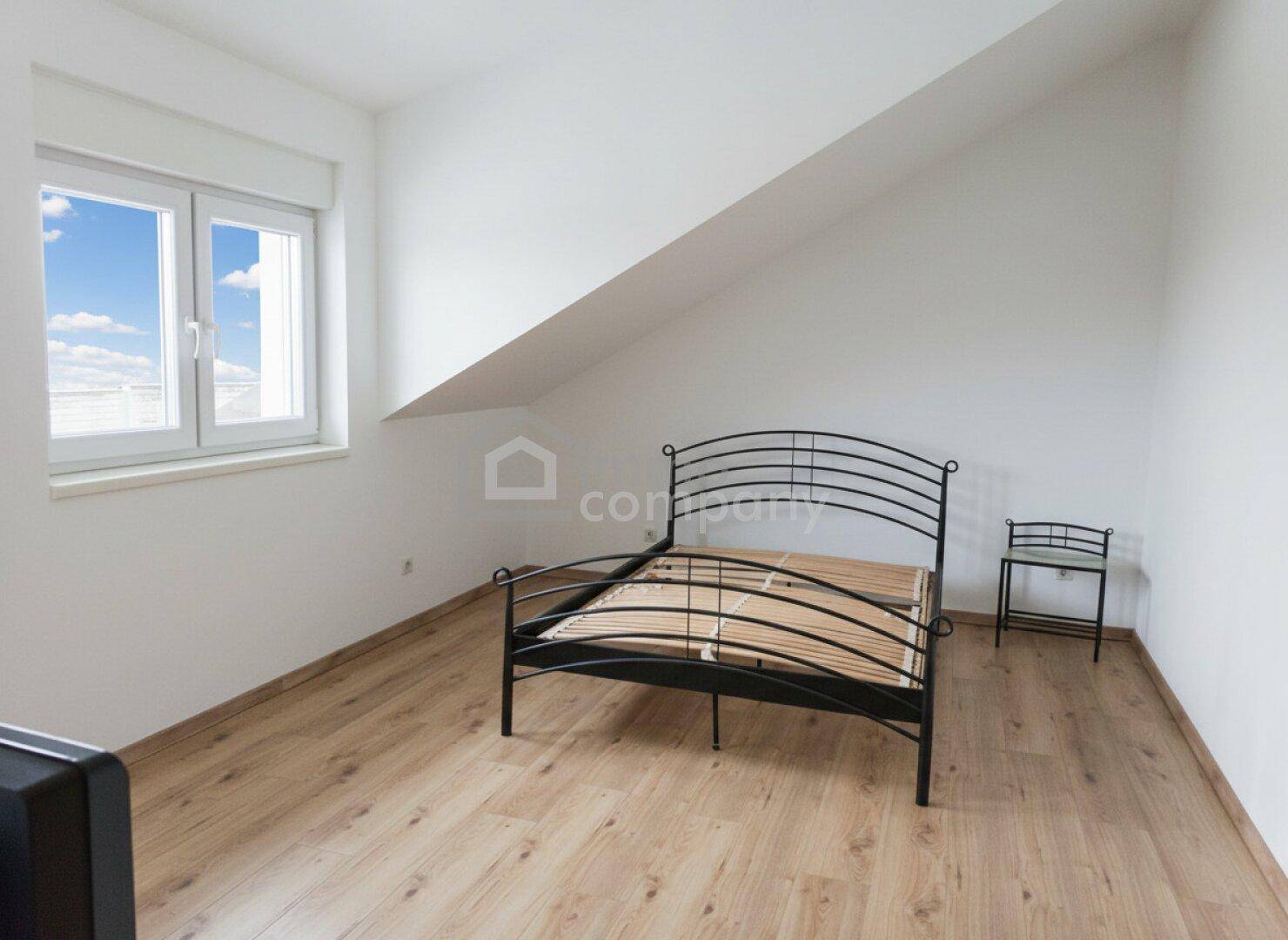 Schlafzimmer im Dachgeschoss mit Holzboden, Dachschräge und einem Fenster mit Blick ins Grüne.