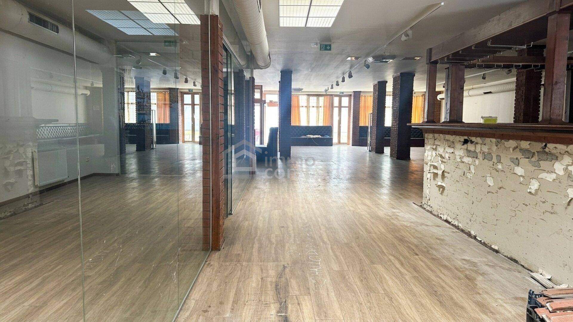 Weitläufiger Innenraum mit Holzboden, Glaswänden und sichtbaren Renovierungsspuren.