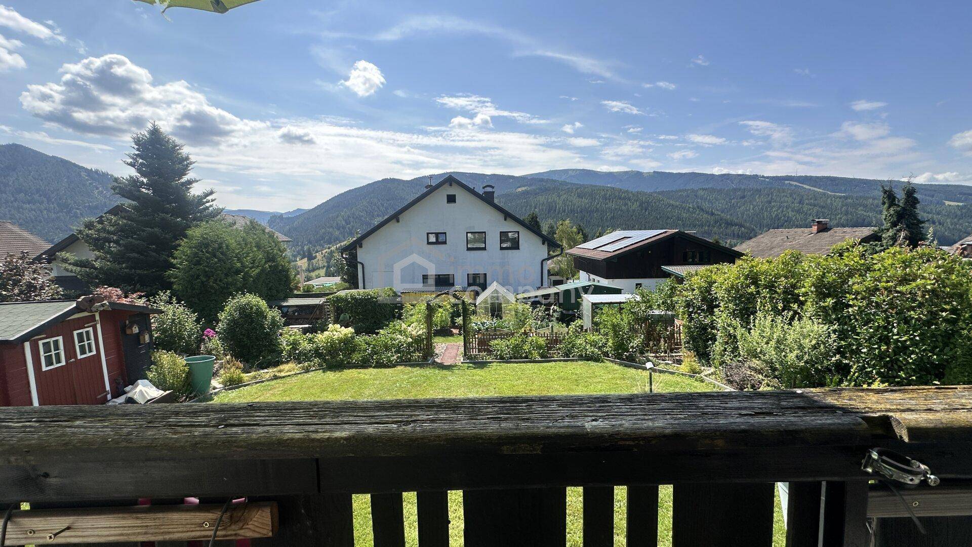Weitblick vom Balkon über den grünen Garten und die malerische Berglandschaft.