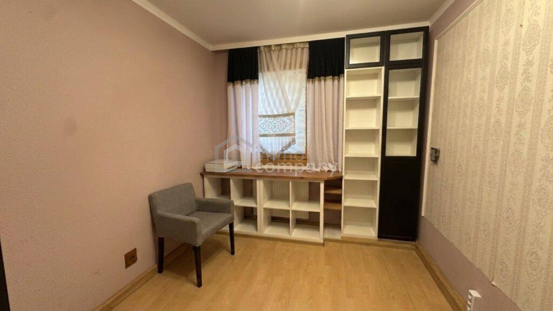 Helles Zimmer mit Regalsystemen, einem Stuhl und einem Fenster, ideal als Arbeits- oder Gästezimmer.
