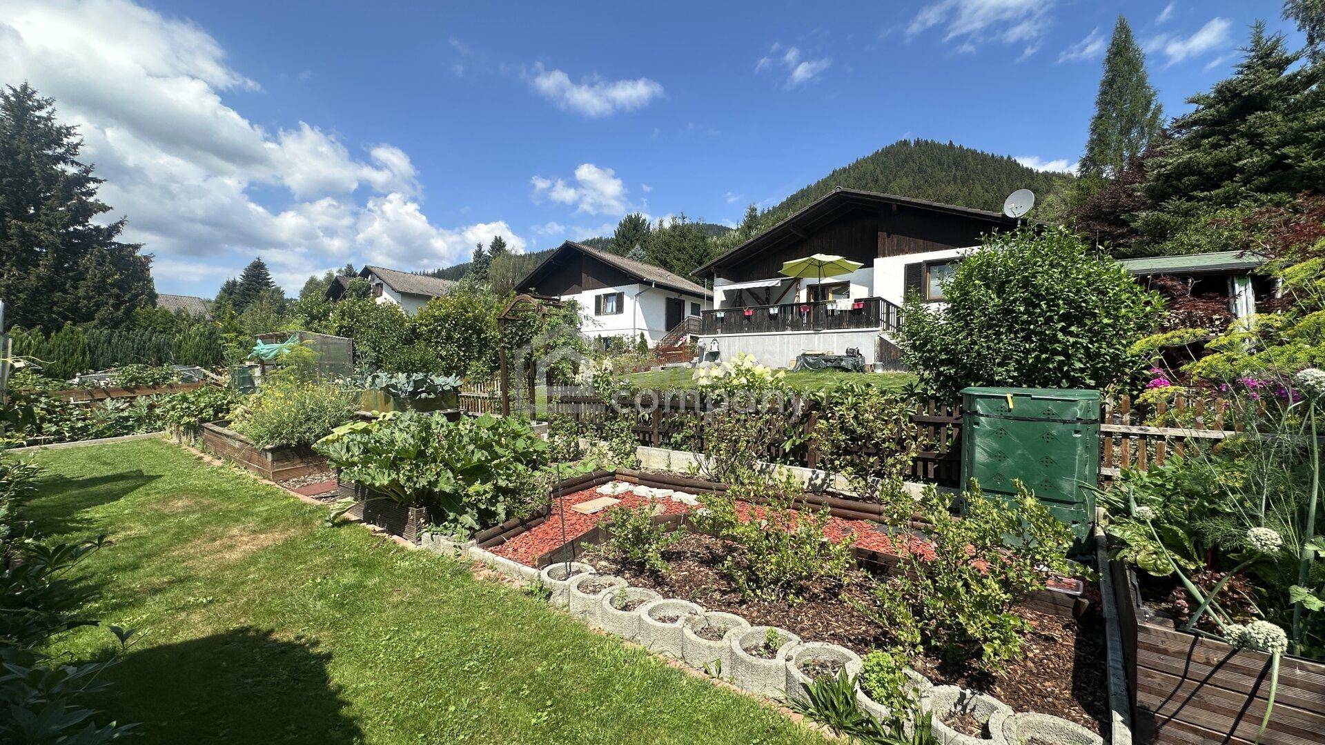Gepflegter Gartenbereich mit Rasenfläche, Hochbeeten und Blick auf die umliegende Berglandschaft.