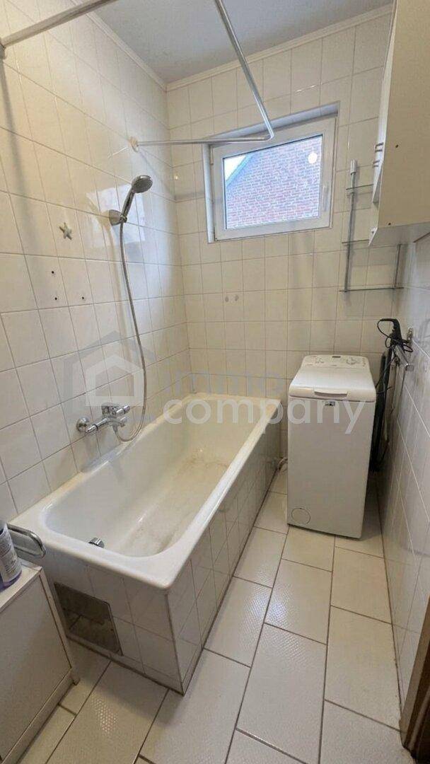 Helles Badezimmer mit Badewanne, Dusche, weißen Fliesen und einer Waschmaschine.