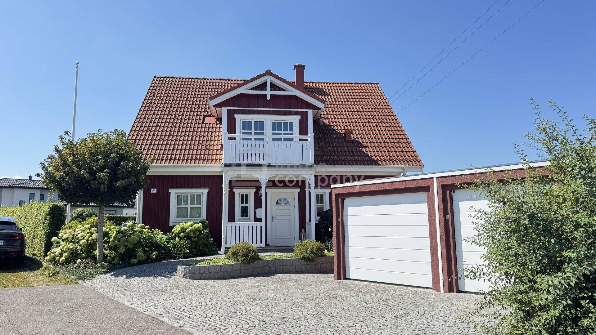 Vorderansicht des roten Hauses mit weißer Fassade, Balkon und einer Doppelgarage.