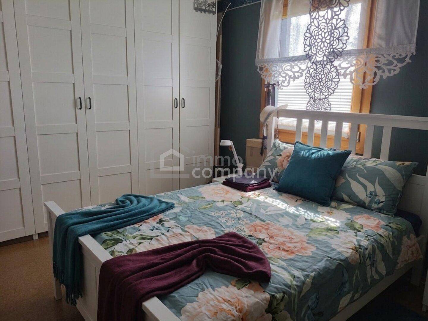 Gemütliches Schlafzimmer mit weißem Bett, floraler Bettwäsche und geräumigen Kleiderschränken.