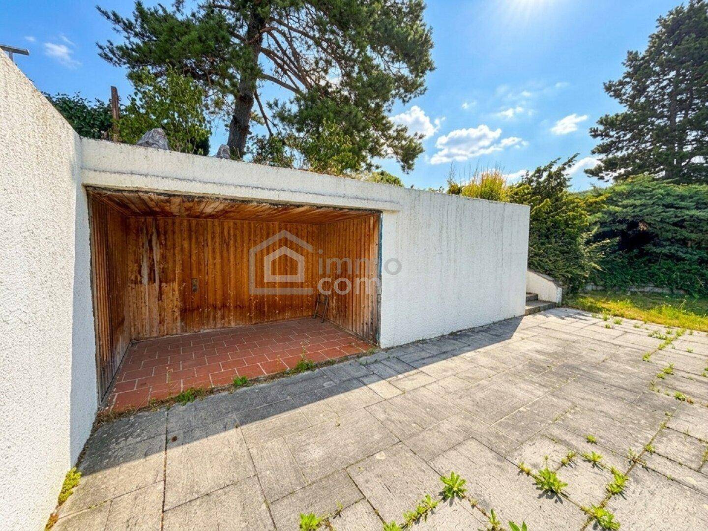 Offene Garage mit Holzwänden und gepflastertem Vorplatz, ideal für Fahrzeuge oder Lagerung.