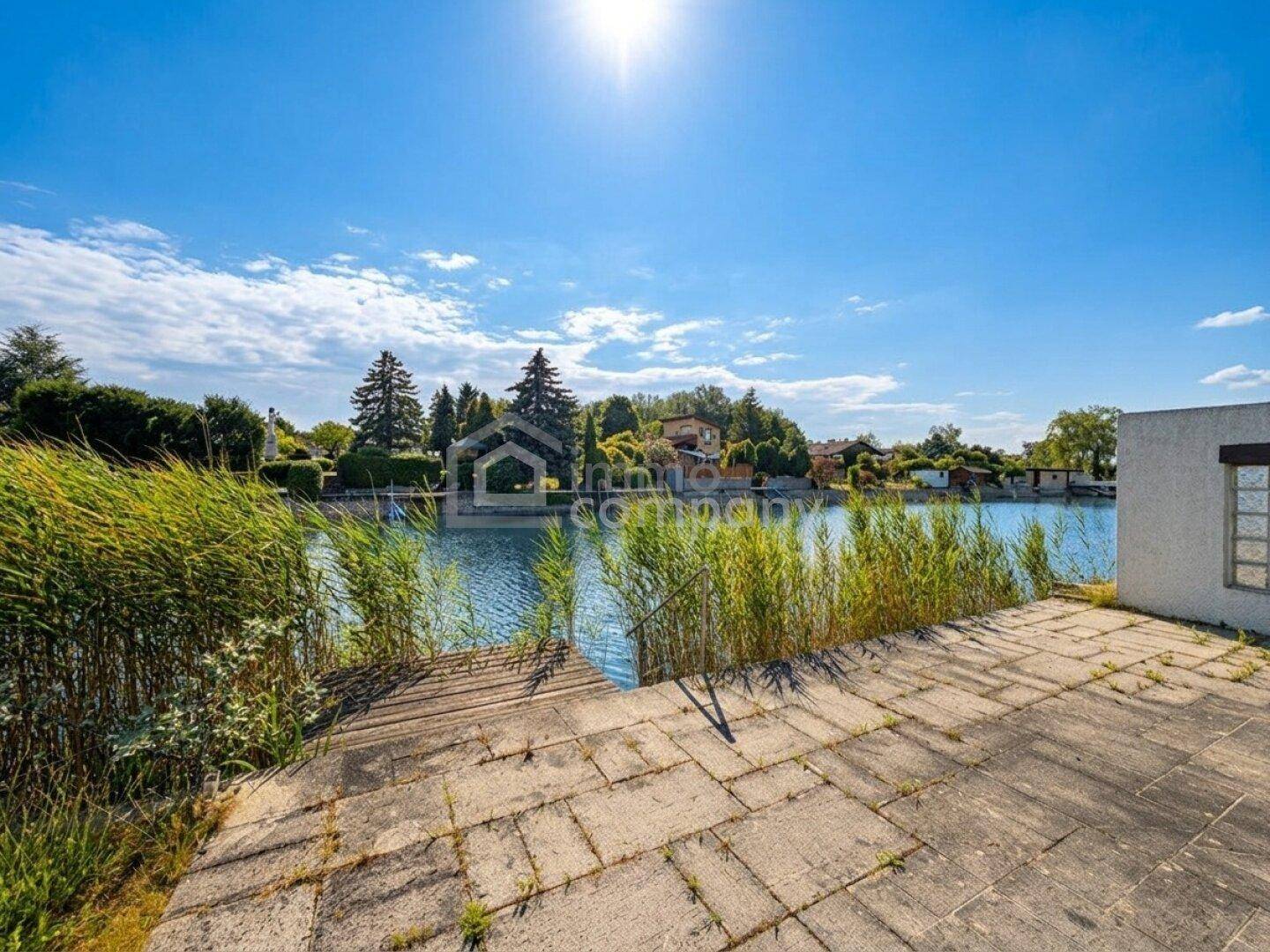 Geräumige Steinterrasse direkt am Wasser mit Schilfbewuchs und weitem Blick über den See.