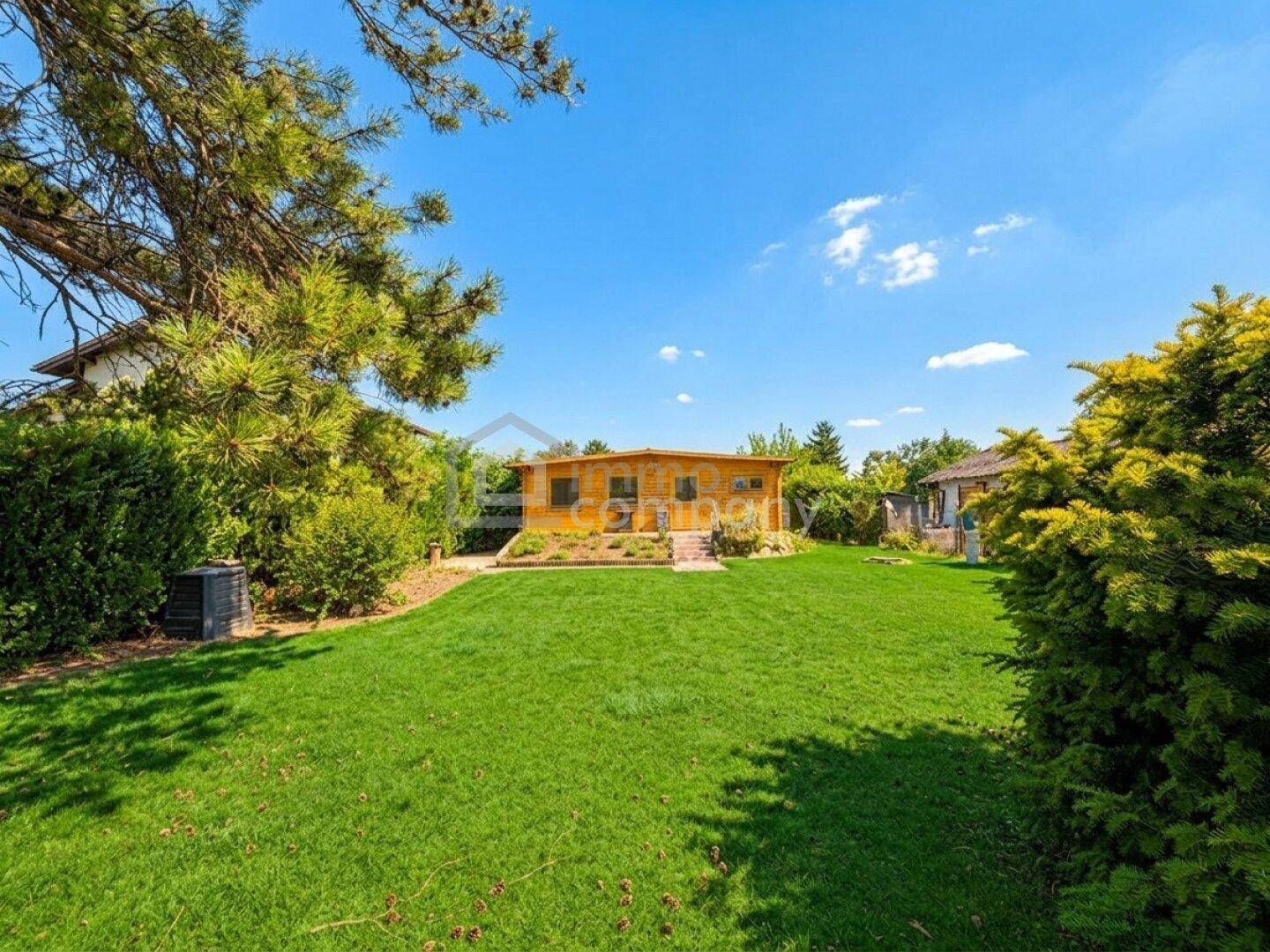 Gepflegter Garten mit weitläufiger Rasenfläche und einem charmanten Holzhaus im hinteren Bereich.