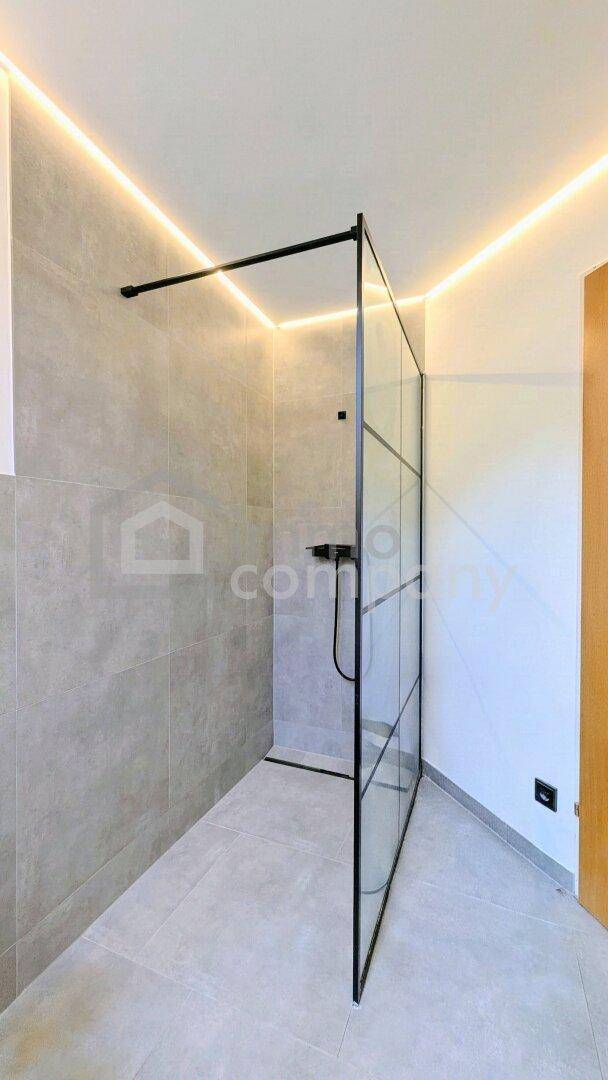 Geräumige begehbare Dusche mit Glasabtrennung und modernen grauen Fliesen.