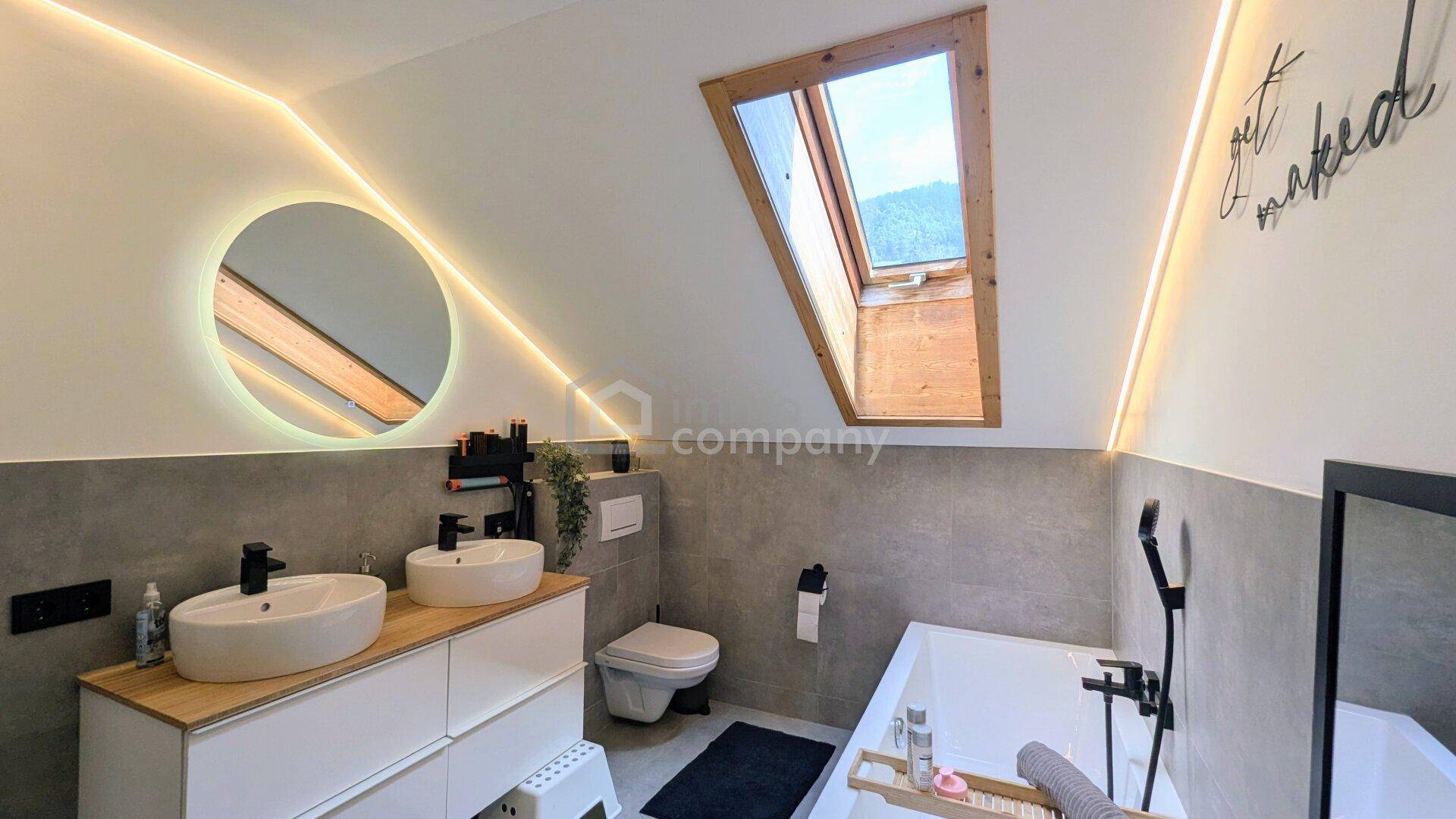 Helles Badezimmer mit Doppelwaschbecken, Toilette, Badewanne und Dachfenster.