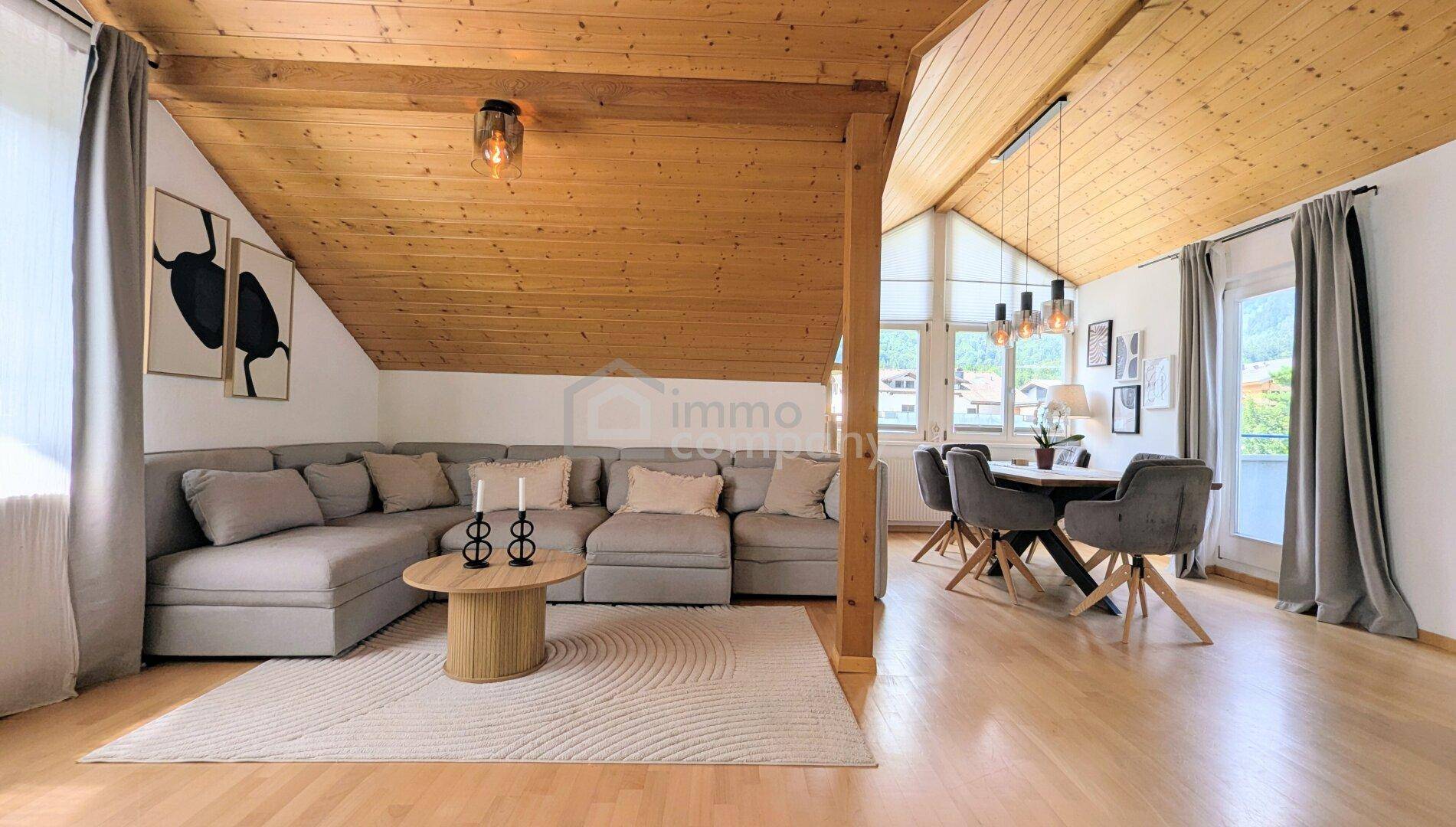 Gemütlicher Wohn- und Essbereich mit großem Ecksofa, Holzbalken und schrägen Decken.