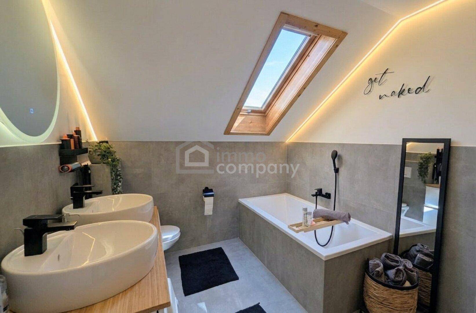 Modernes Badezimmer mit Doppelwaschbecken, Badewanne, Dachfenster und indirekter Beleuchtung.