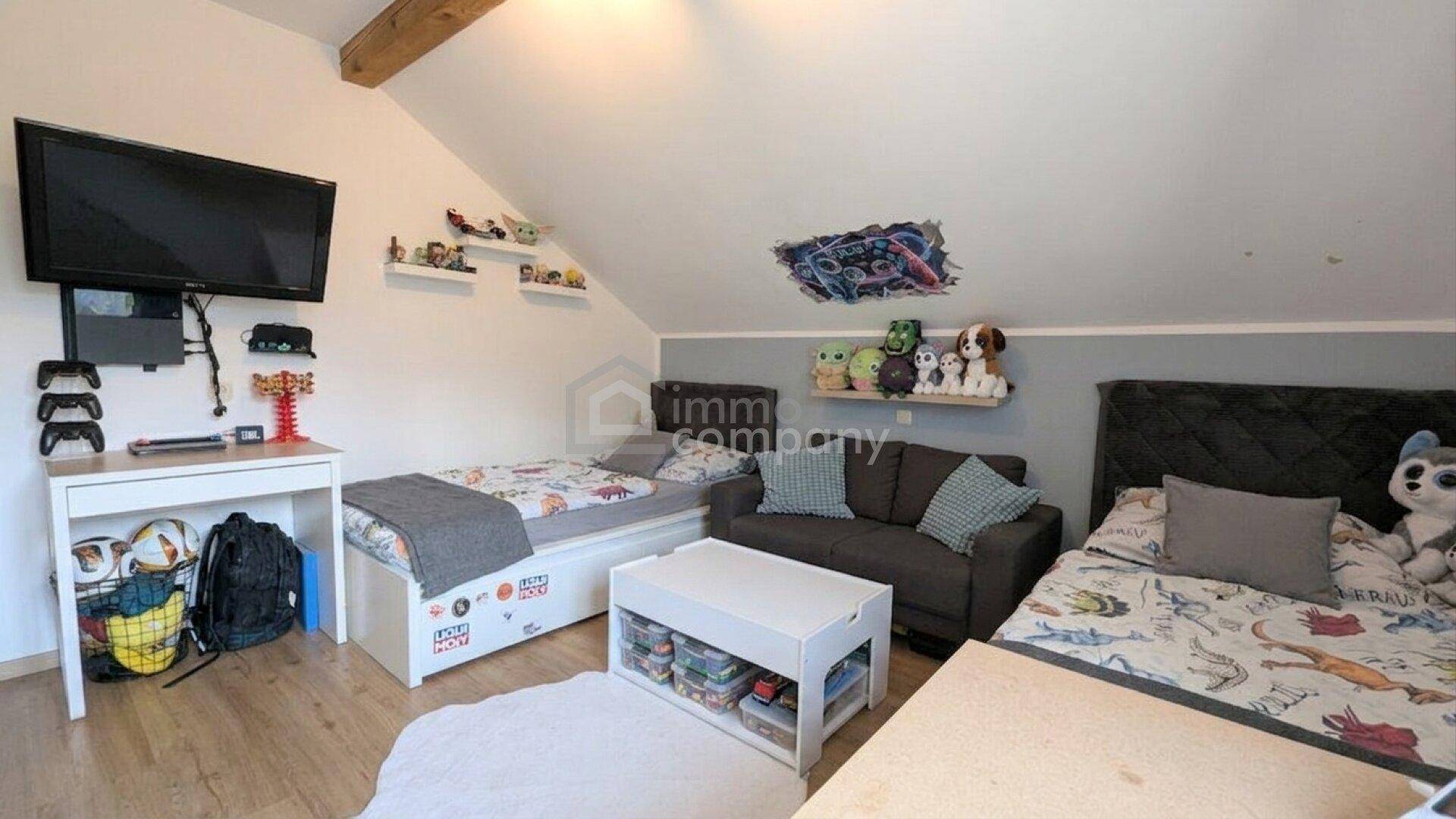 Geräumiges Kinderzimmer mit zwei Betten, Sofa, Fernseher und schräger Decke.