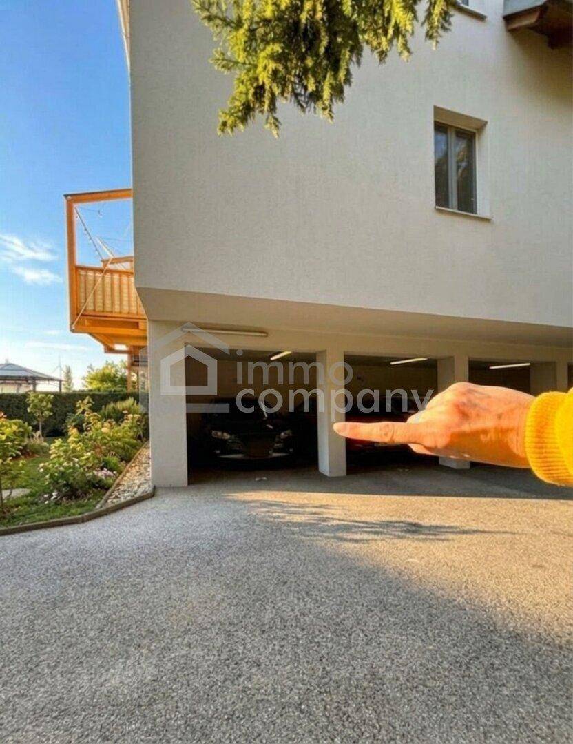 Modernes Gebäude mit überdachtem Parkplatz, gepflegtem Garten und Holzbalkon.