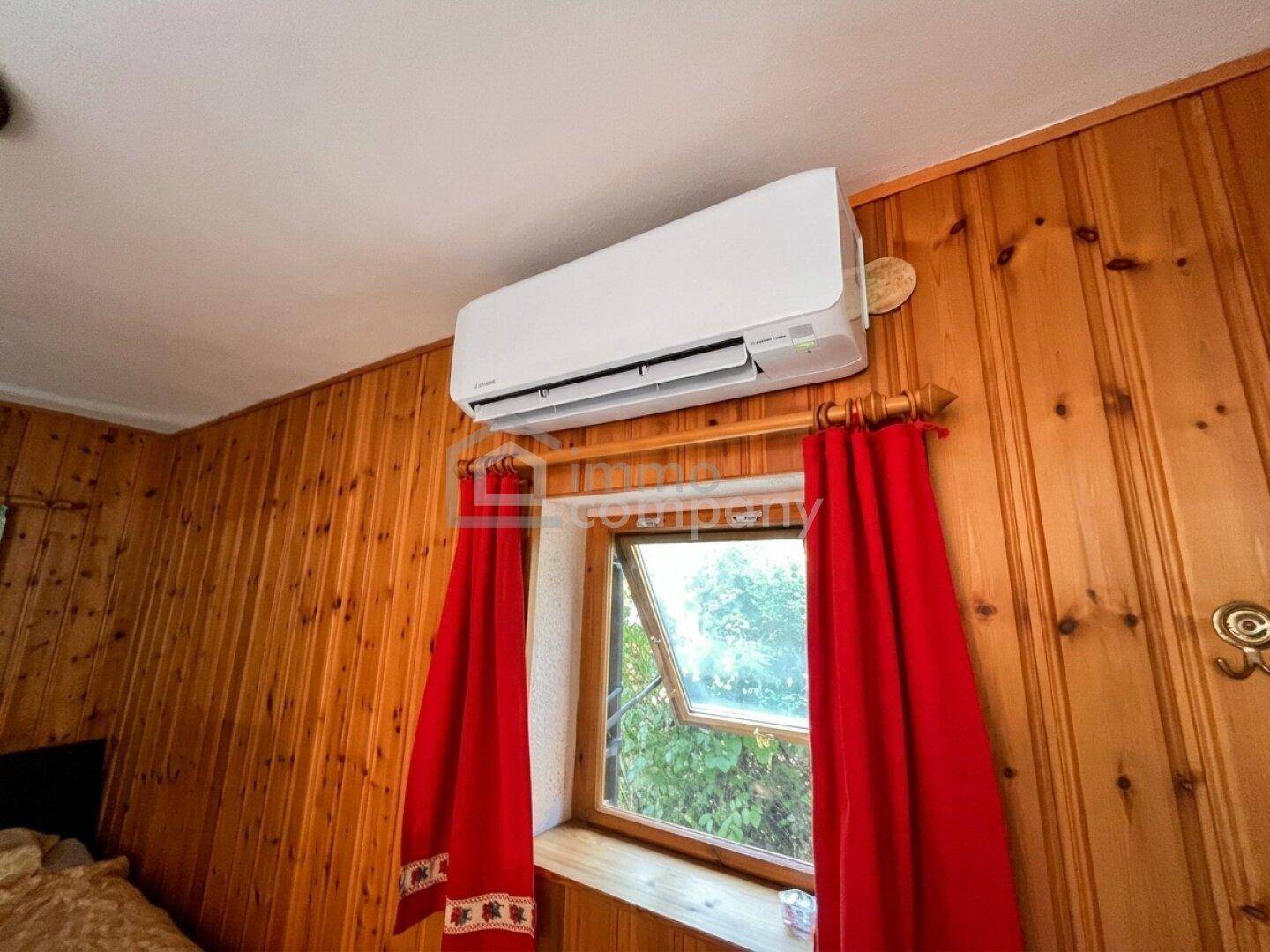 Schlafzimmer mit Holzwänden, einem Fenster und einer Klimaanlage an der Decke.
