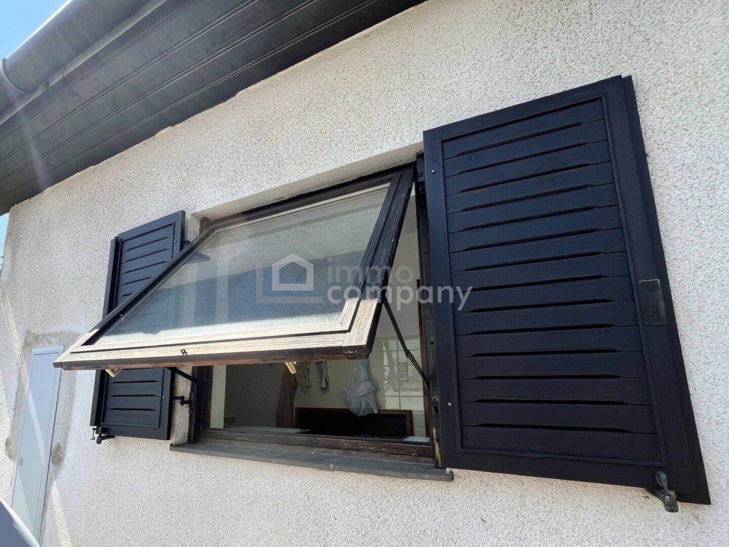 Außenansicht eines Fensters mit geöffneten schwarzen Fensterläden an einer strukturierten Fassade.