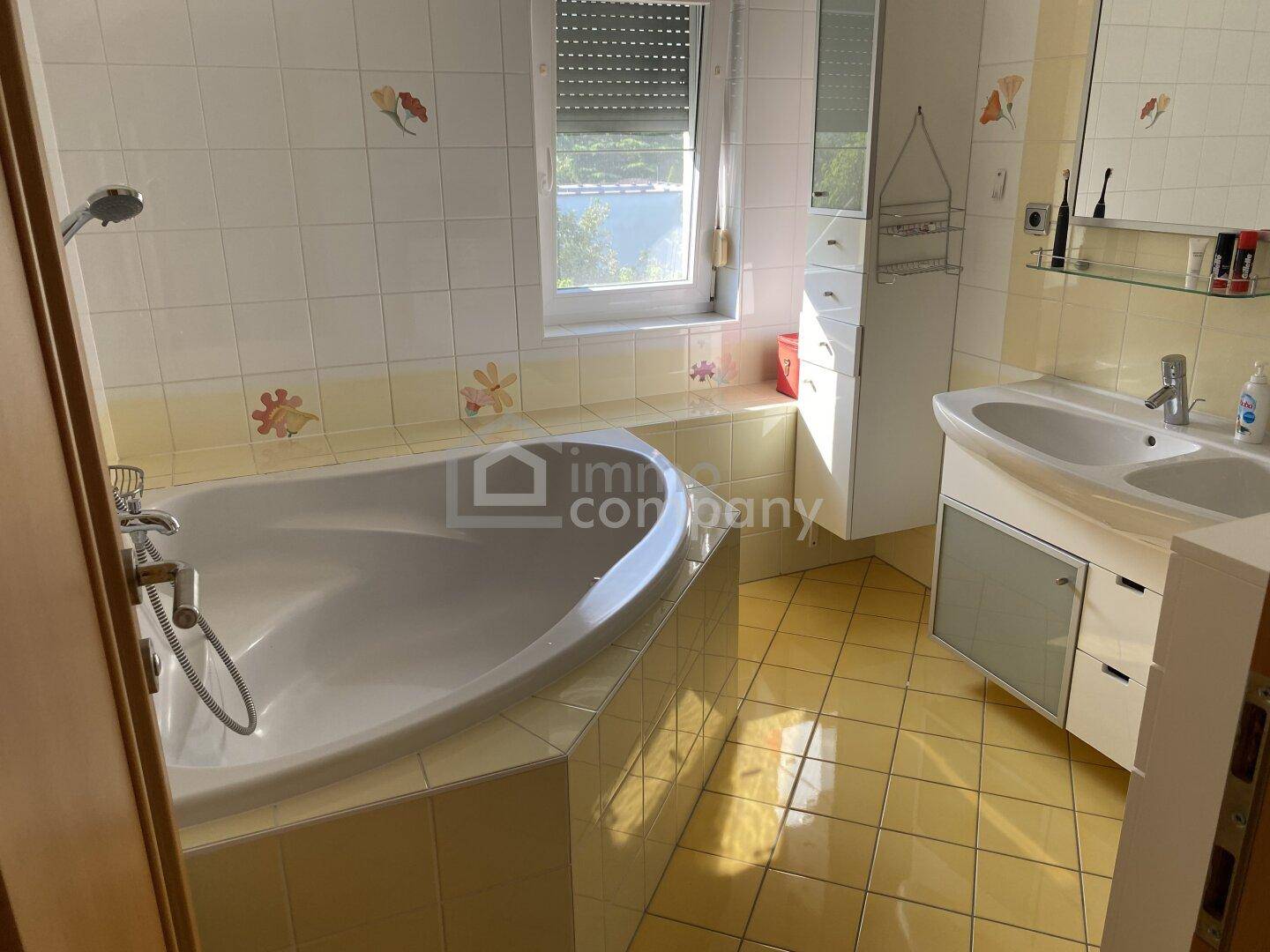 Helles Badezimmer mit gelben Fliesen, einer Badewanne und einem Waschbecken mit Unterschrank.
