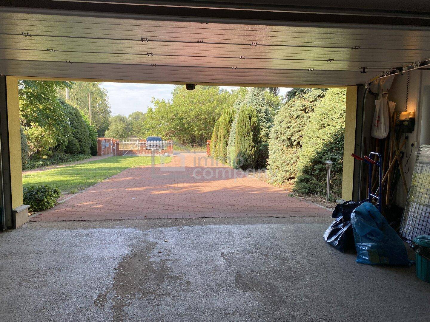 Blick aus der Garage auf die gepflasterte Einfahrt und den grünen Gartenbereich.