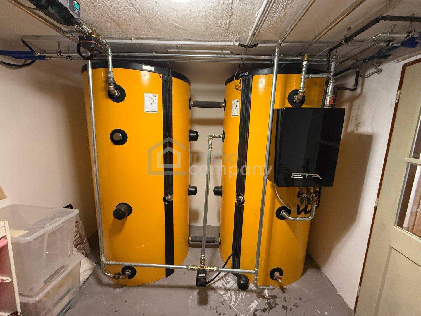 Technikraum mit zwei großen Warmwasserspeichern und sichtbaren Rohrleitungen.