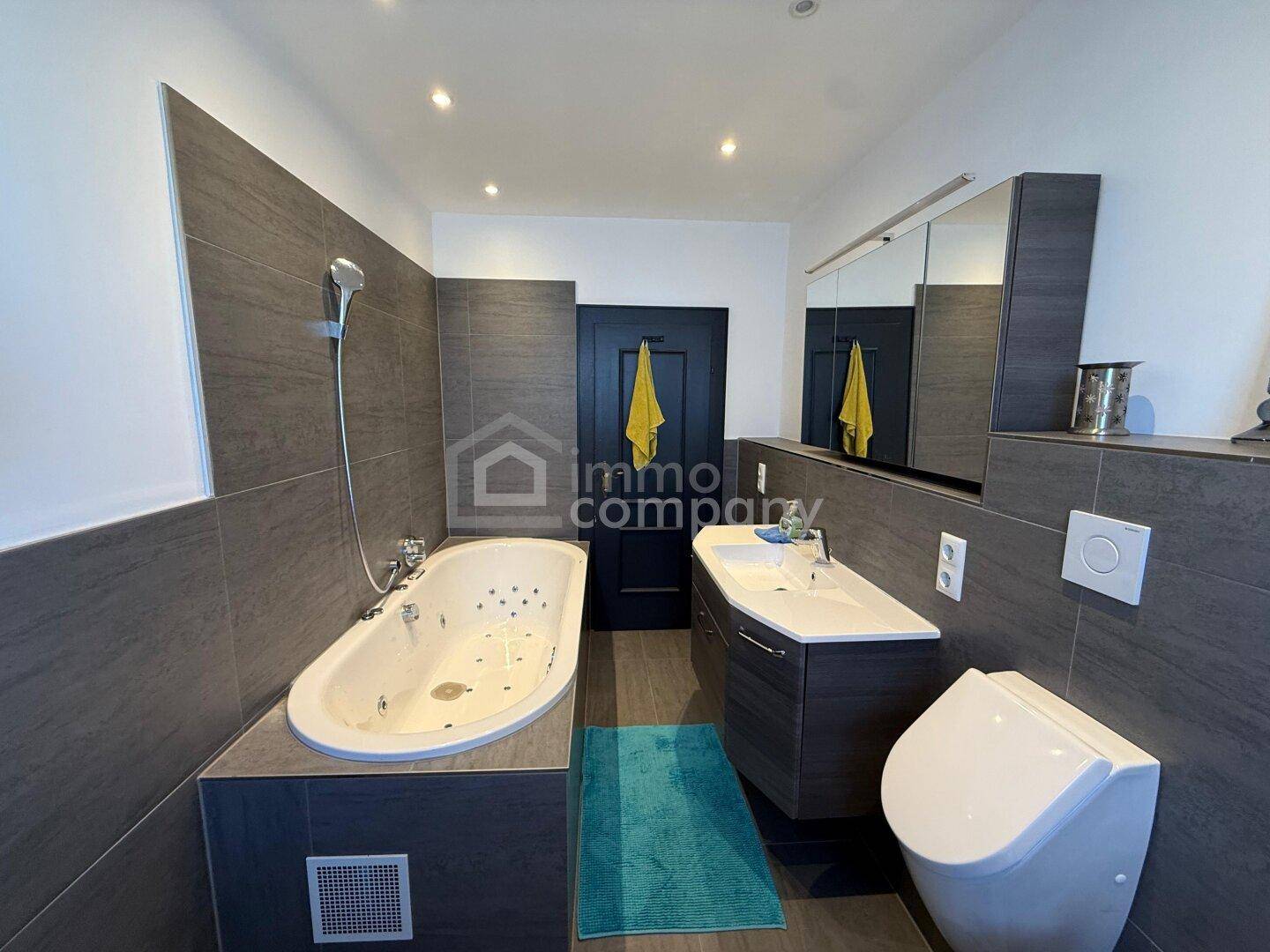 Modernes Badezimmer mit Badewanne, Einzelwaschbecken und dunklen Fliesen an Wänden und Boden.