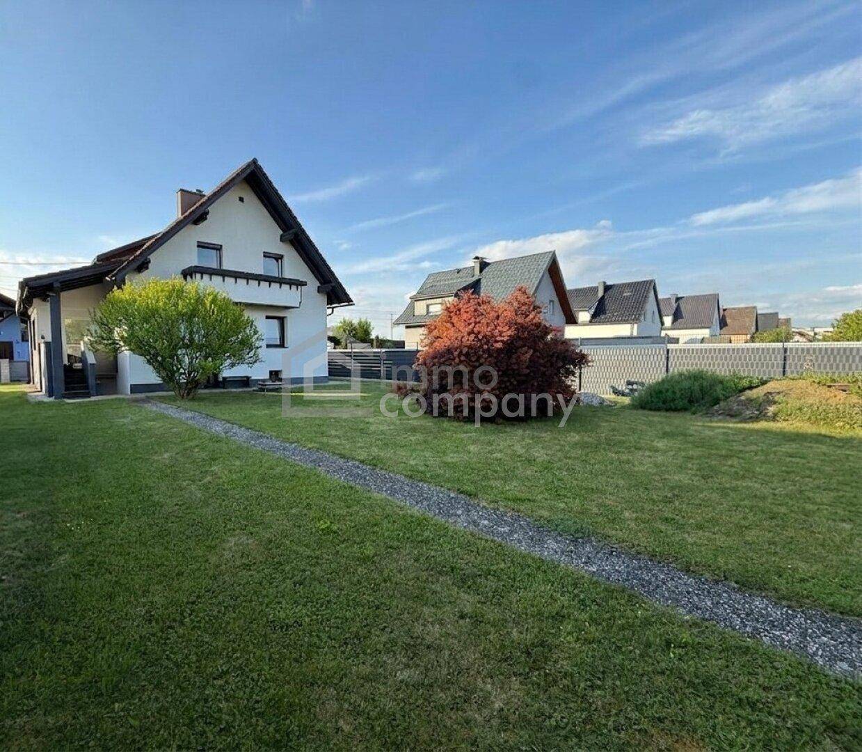 Großzügiger Gartenbereich mit Rasenfläche und Blick auf das moderne Einfamilienhaus bei Sonnenschein.