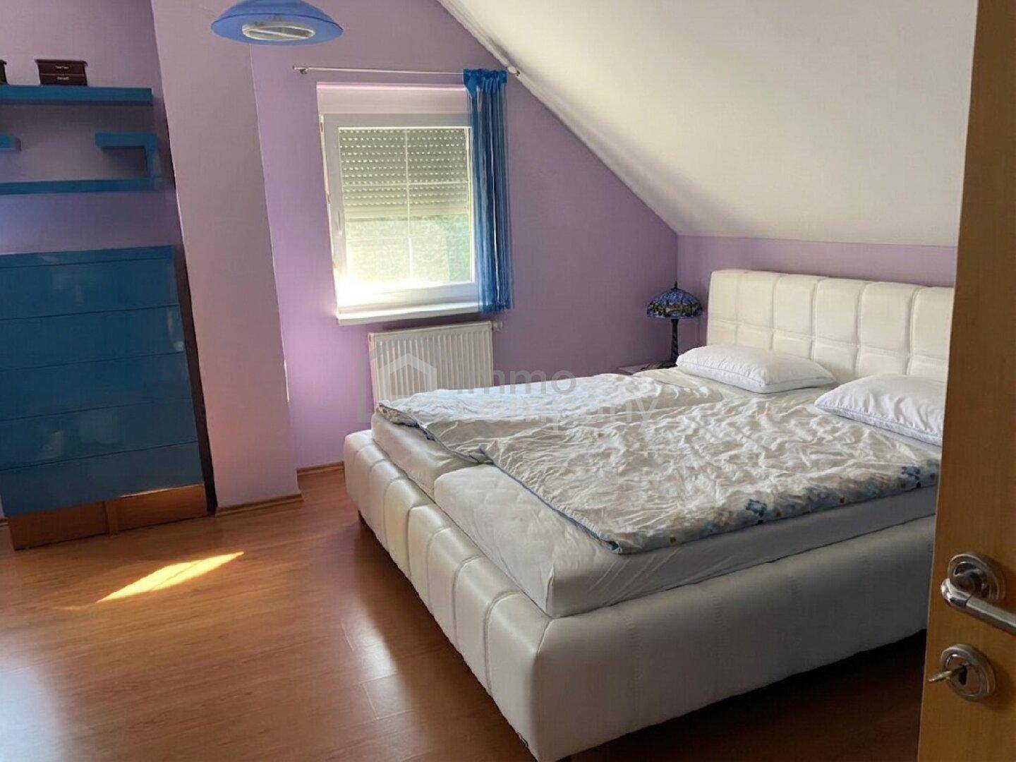 Schlafzimmer mit Dachschräge, Doppelbett und lila Wänden, bietet eine gemütliche und farbenfrohe Atmosphäre.