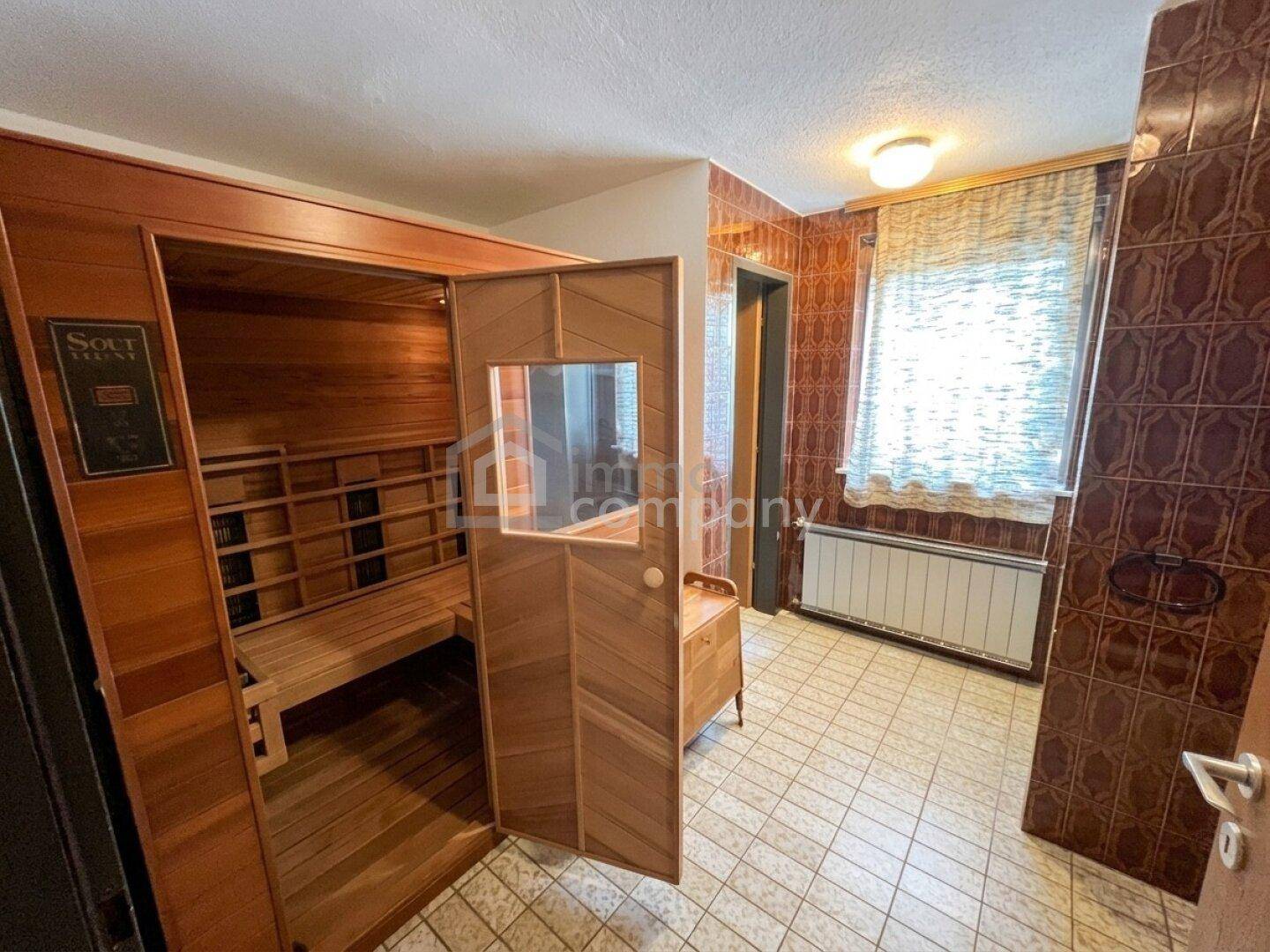 Badezimmer mit einer integrierten Sauna, braunen Fliesen und einem Heizkörper, der für Wärme sorgt.