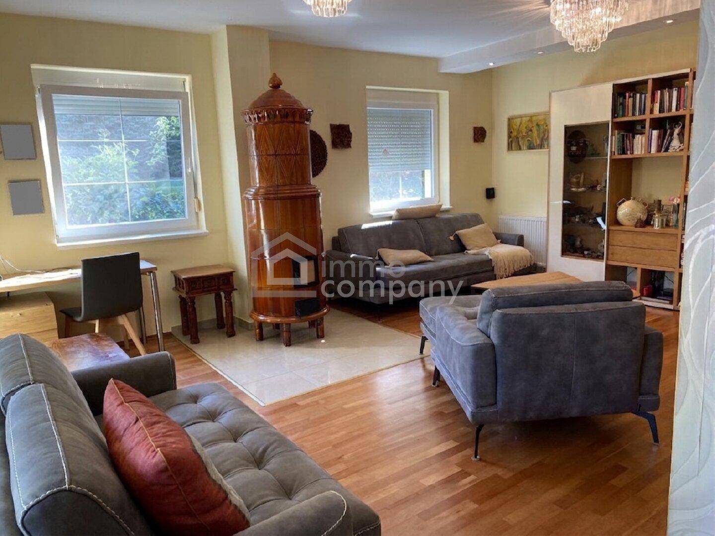 Helles Wohnzimmer mit traditionellem Kachelofen, Parkettboden und bequemen Sofas, bietet eine gemütliche Atmosphäre.
