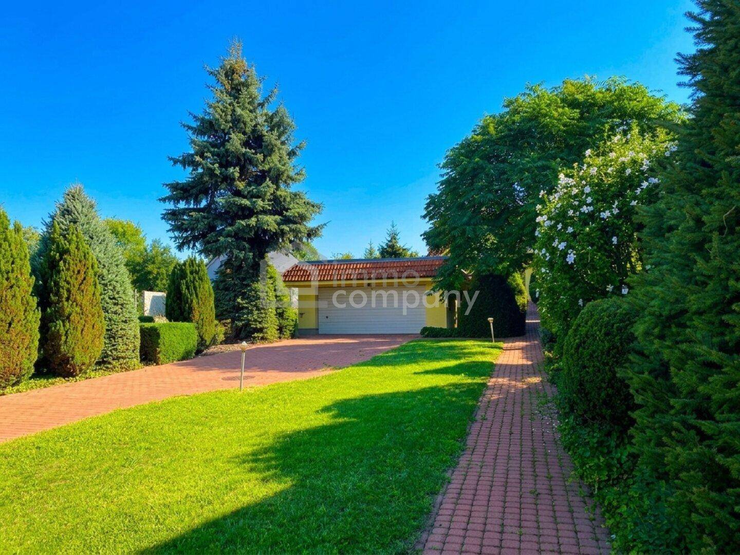 Gepflegte Auffahrt mit Rasenfläche und Bäumen führt zur Doppelgarage des Hauses unter blauem Himmel.