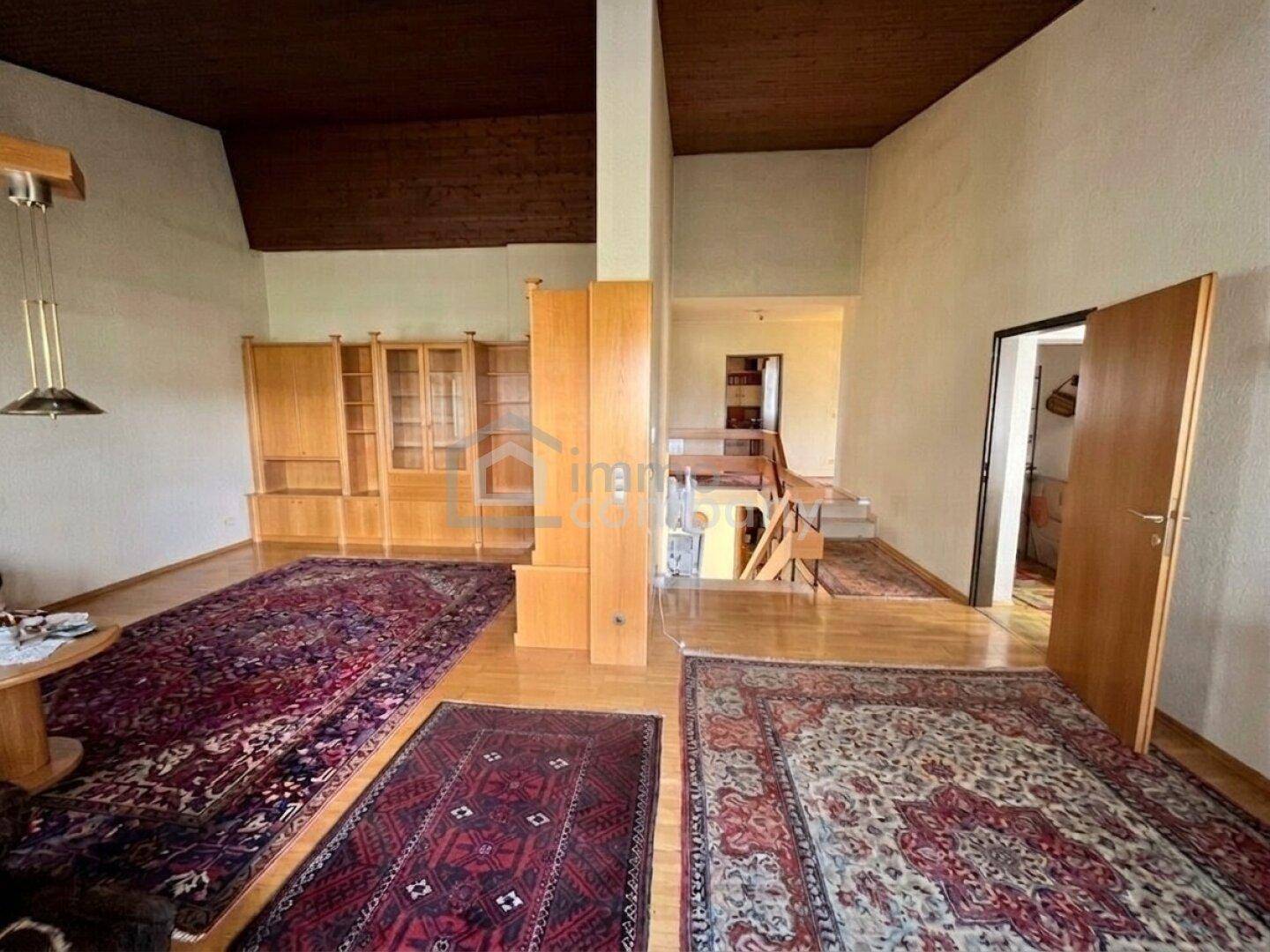 Geräumiges Wohnzimmer mit Holzboden, hohen Decken und einem offenen Zugang zu einer Treppe.