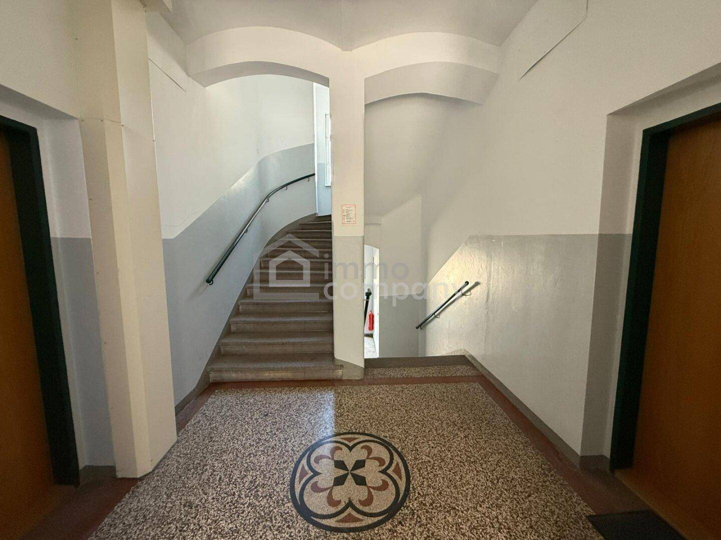 Geräumiges Treppenhaus mit Terrazzoboden und geschwungenen Treppen in einem Altbau.