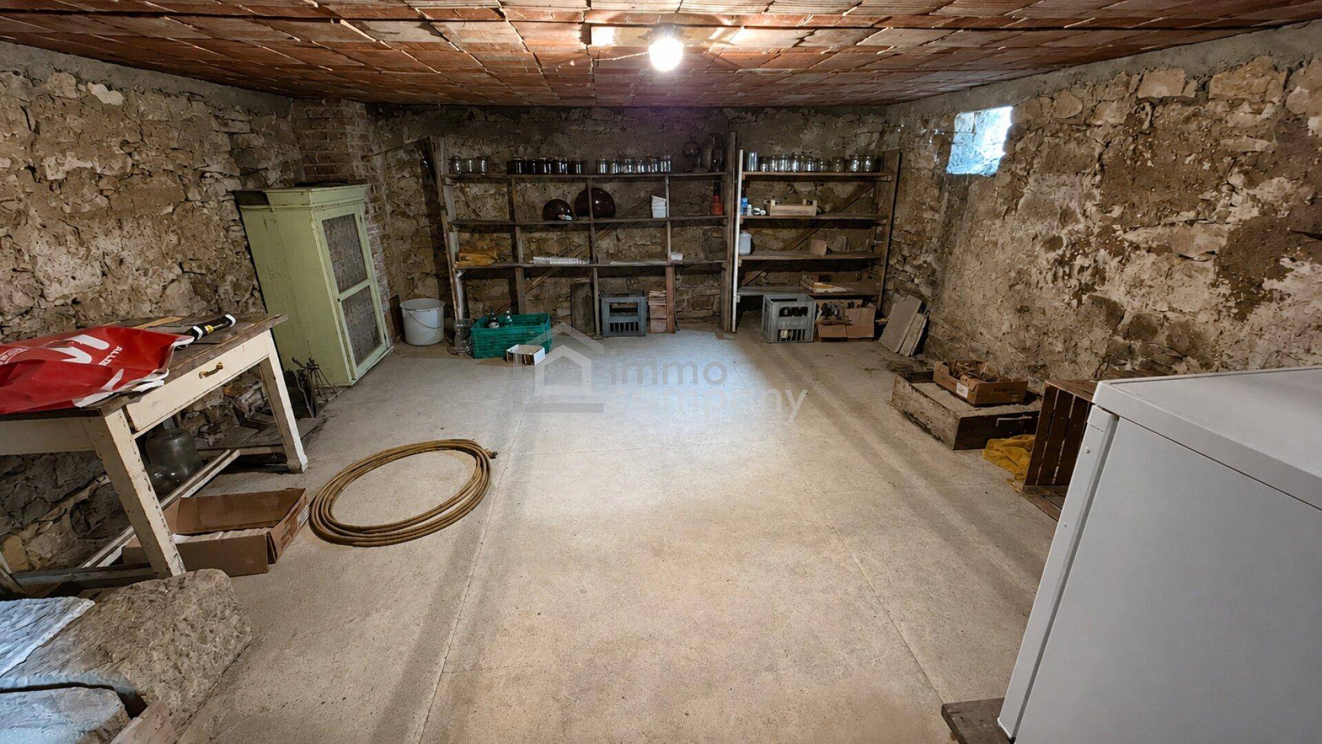 Geräumiger Kellerraum mit unverputzten Steinwänden, Betonboden und Regalen für Lagerzwecke.