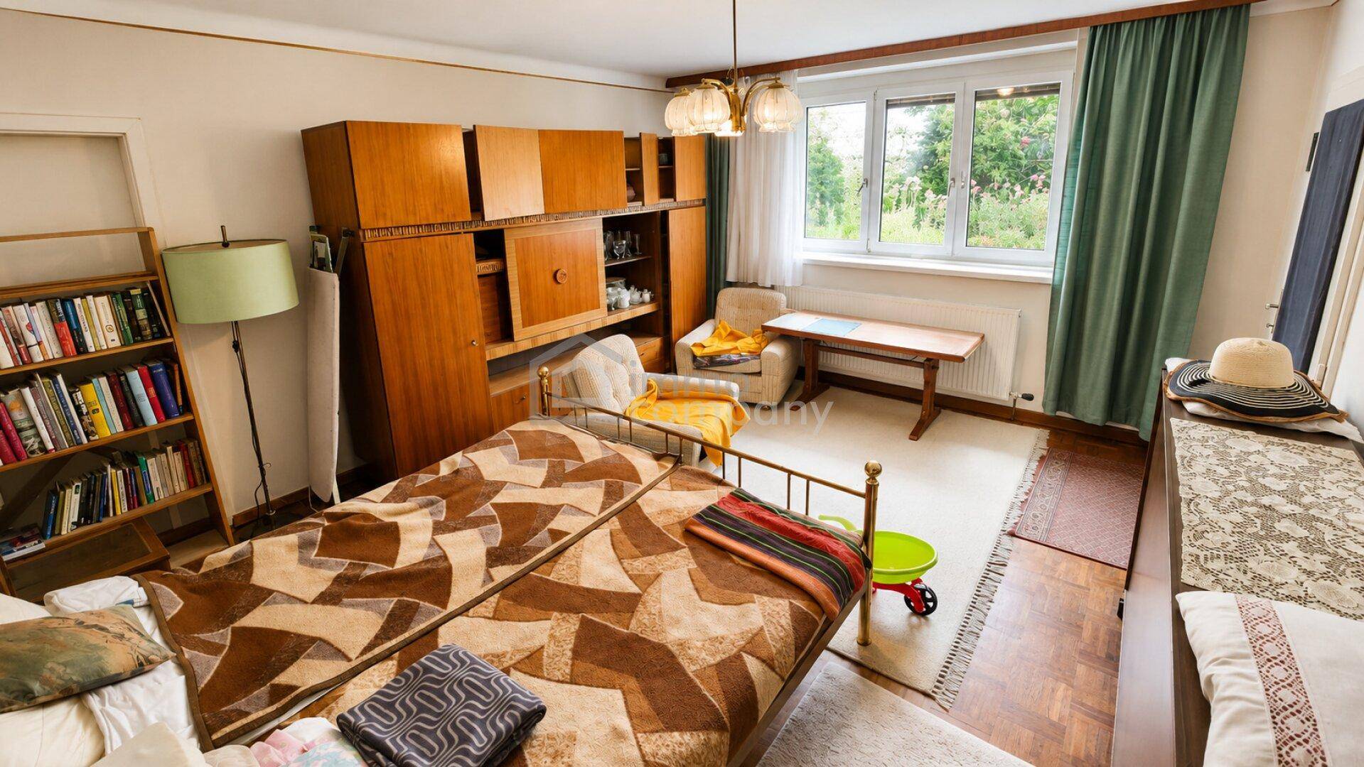 Schlafzimmer mit Bett, großem Holzschrank, Bücherregal und Fenster mit Blick ins Grüne.