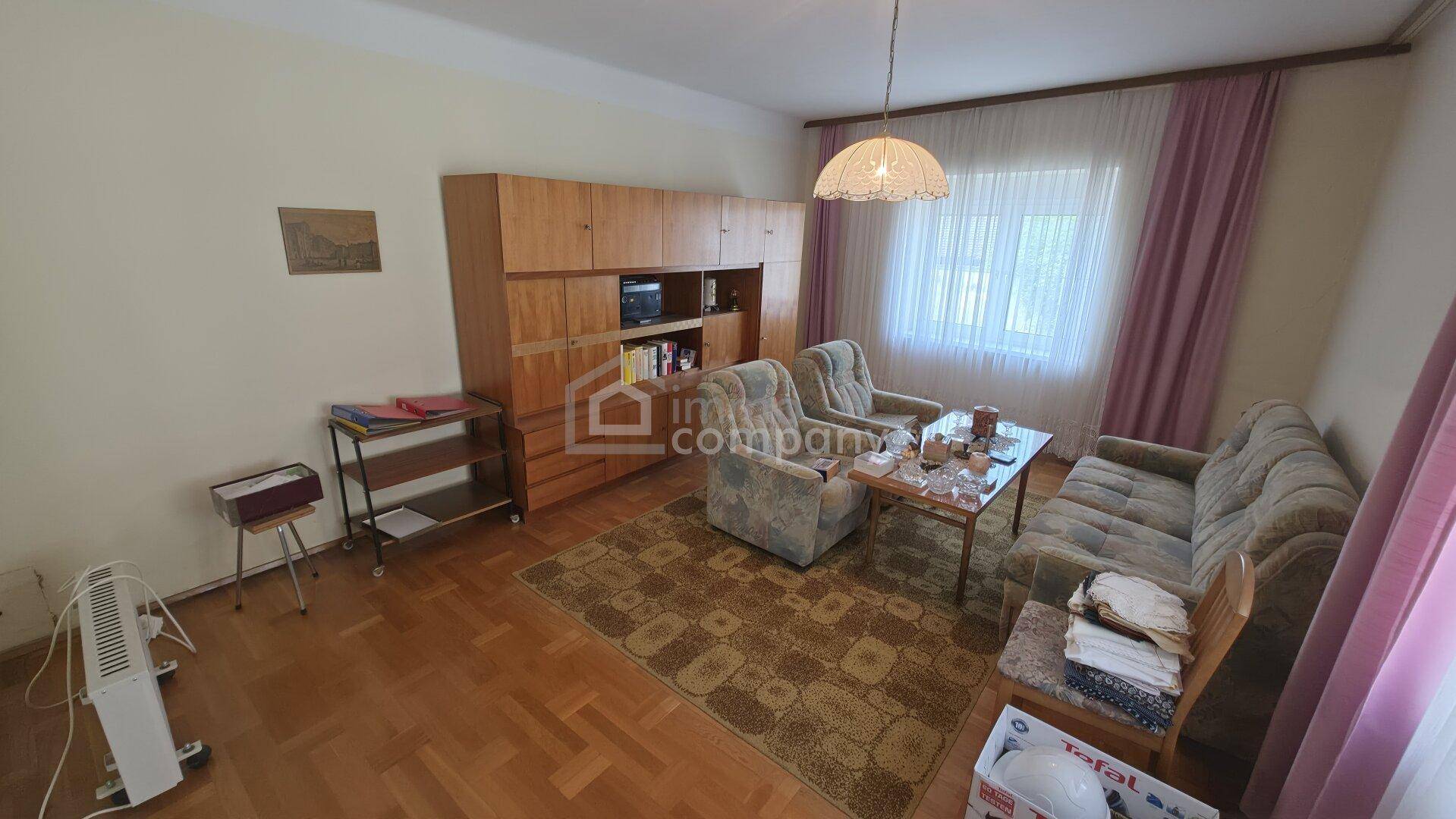 Wohnzimmer mit Sofa, Sesseln, Couchtisch und einem großen Holzschrank.