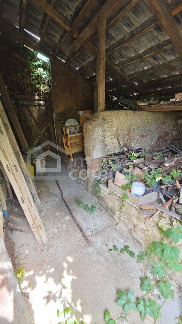 Unausgebauter Dachboden mit sichtbaren Holzbalken, Schutt und einem kleinen Fenster.