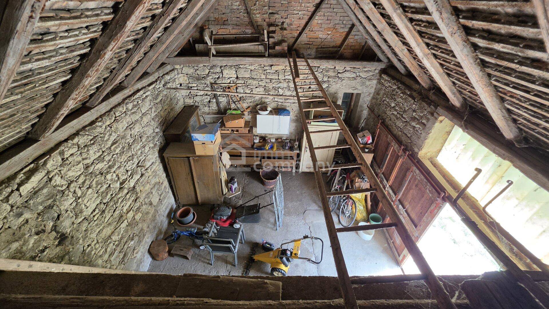 Großer unausgebauter Dachboden mit sichtbaren Holzbalken, Steinwänden und einer Leiter.