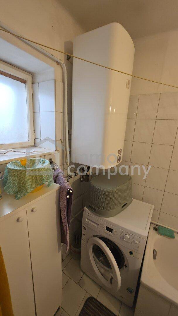 Badezimmer mit Waschmaschine, Warmwasserboiler und einem Fenster für Belüftung.