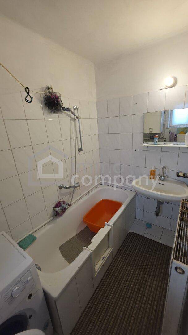 Badezimmer mit Badewanne, Waschbecken und weiß gefliesten Wänden und Boden.