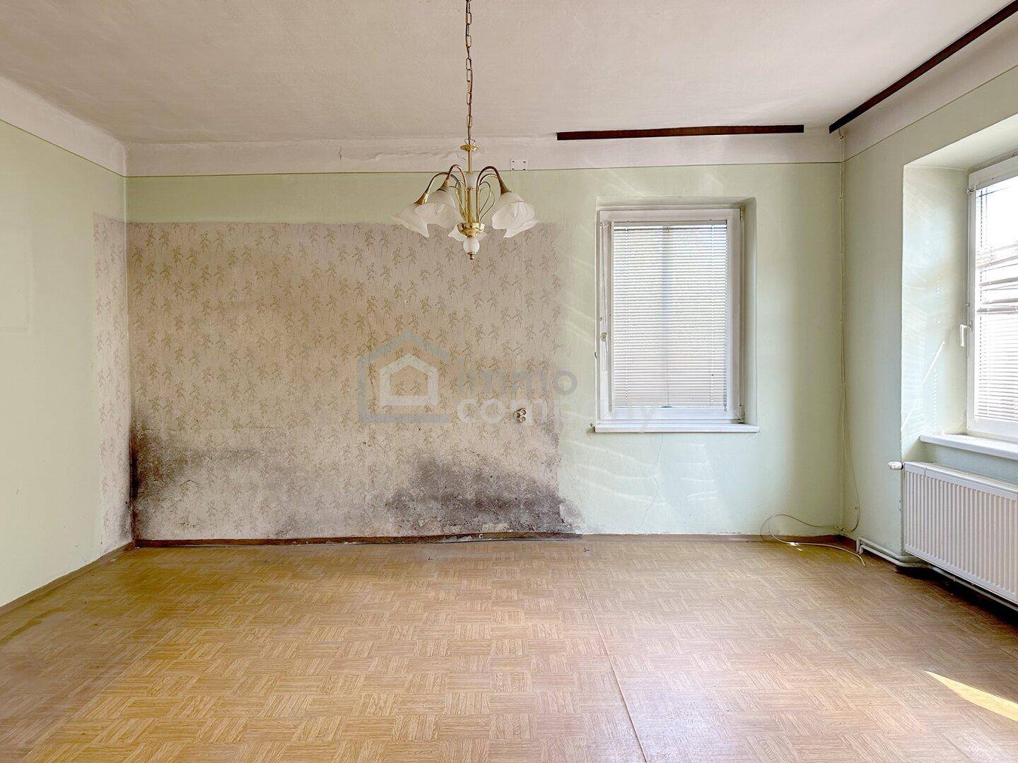 Geräumiger Wohnraum mit abblätternder Tapete, Parkettboden und Kronleuchter.