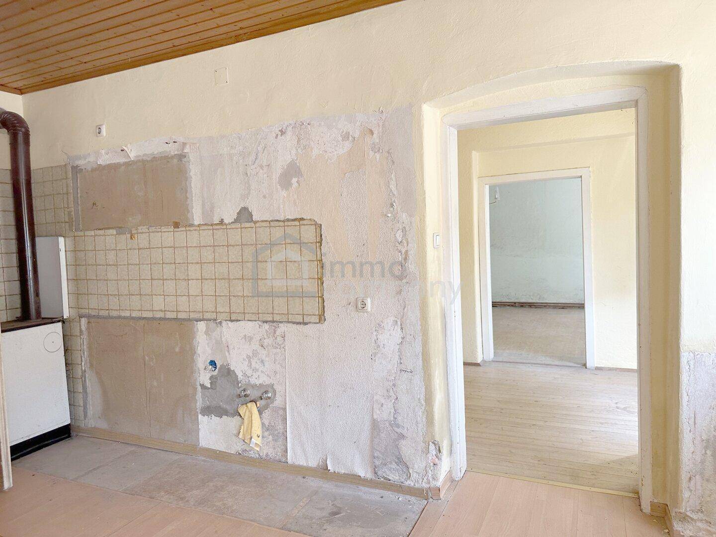 Raum mit Holzbalkendecke, freigelegter Wand und Durchgang zu einem weiteren Zimmer.
