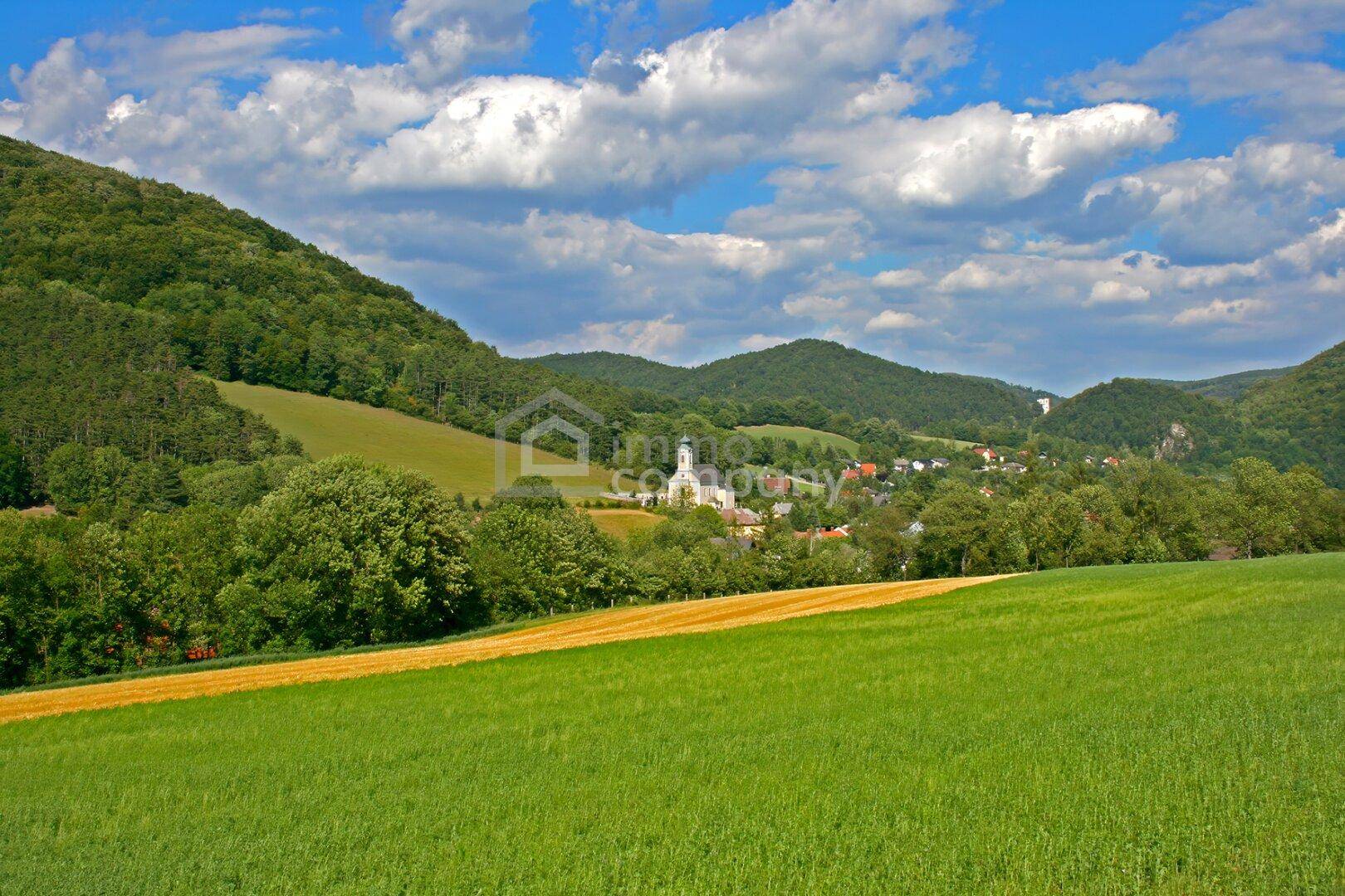 Malerische Landschaft mit grünen Hügeln, einem Dorf und einer Kirche in der Ferne.
