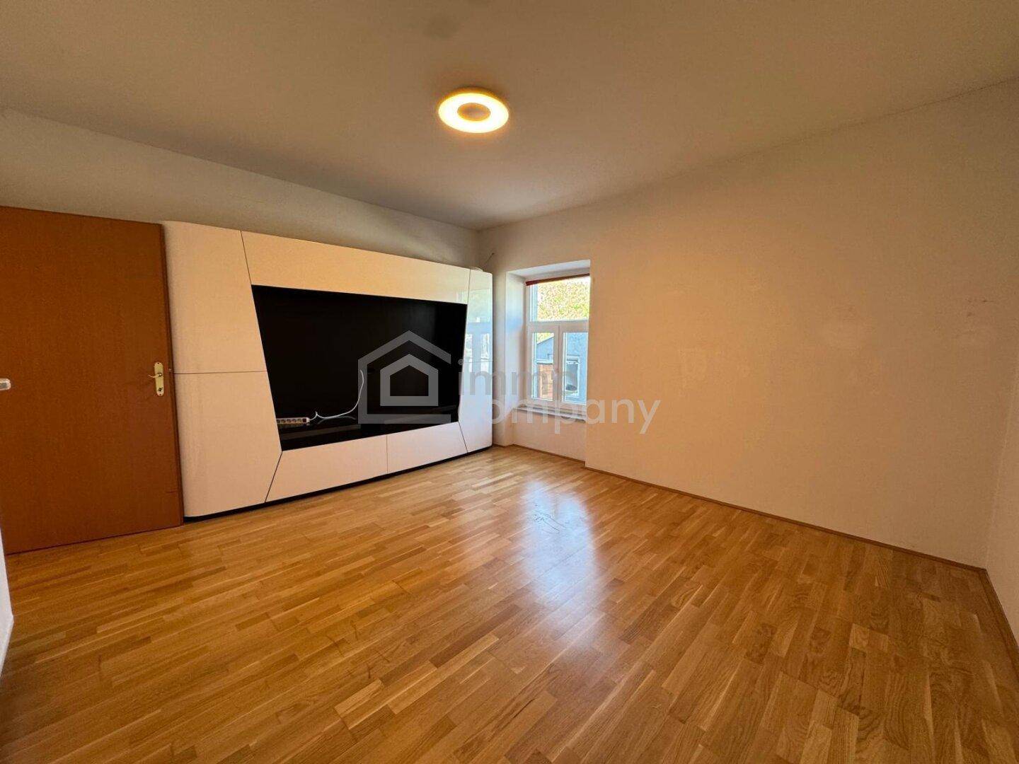 Geräumiges Wohnzimmer mit Parkettboden, einer modernen Medienwand und einem Fenster.