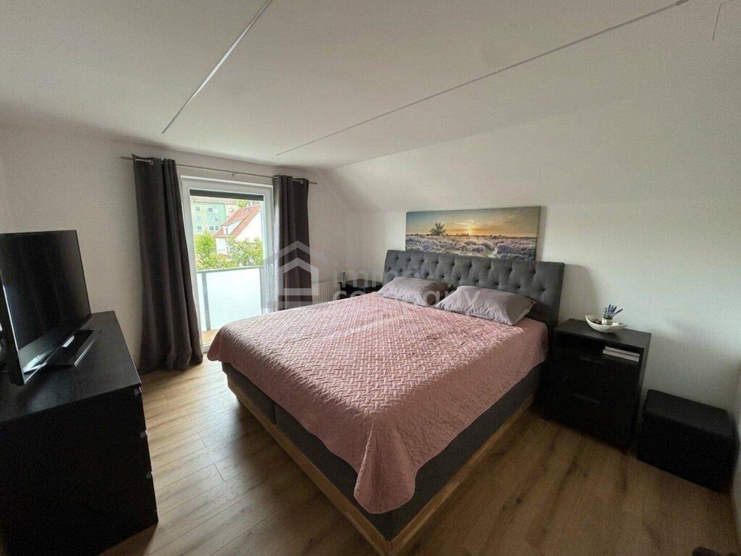 Gemütliches Schlafzimmer mit Doppelbett, Laminatboden und Zugang zu einem kleinen Balkon.