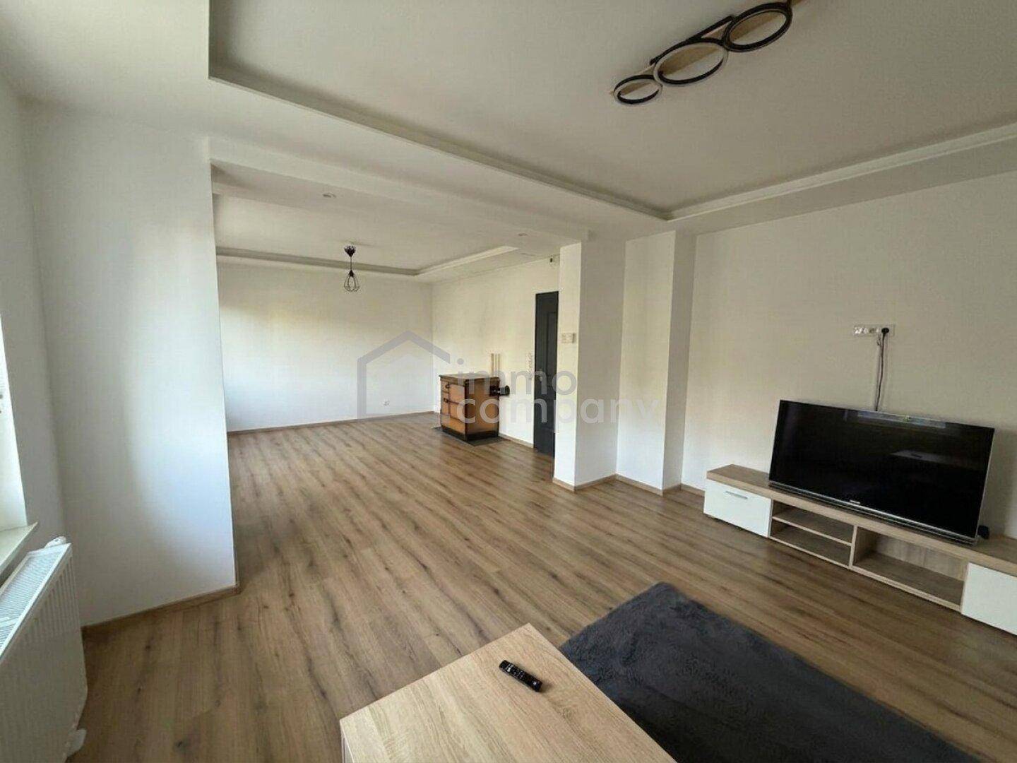 Geräumiges Wohnzimmer mit Laminatboden, TV-Bereich und moderner Deckenbeleuchtung.