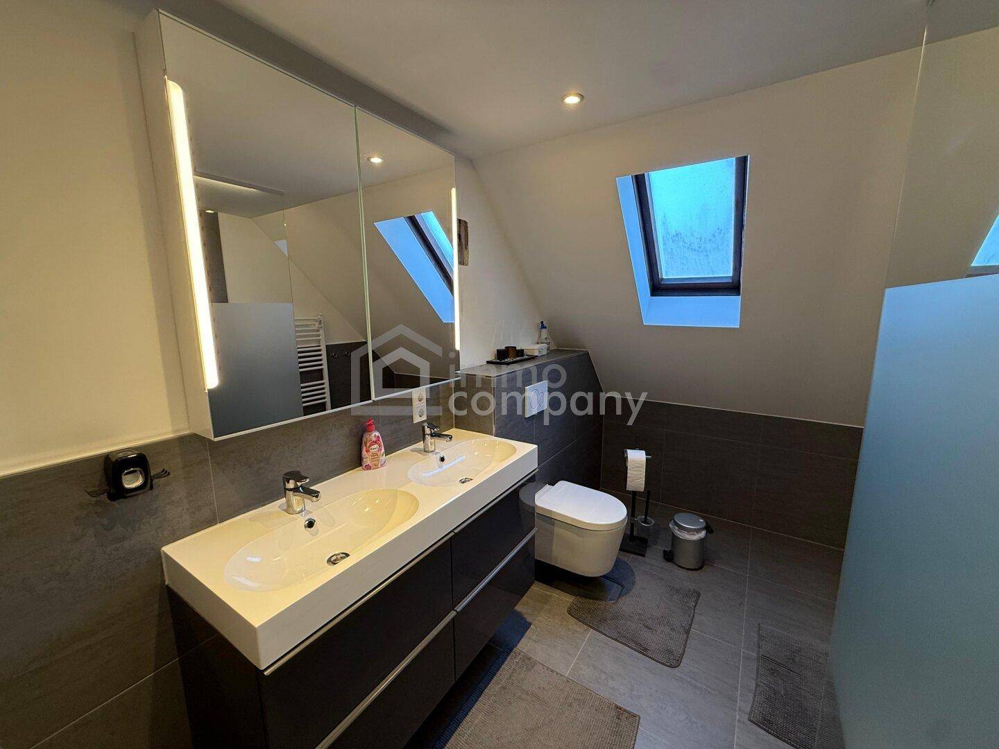 Modernes Badezimmer mit Doppelwaschbecken, Toilette und Dachfenstern für natürliches Licht.
