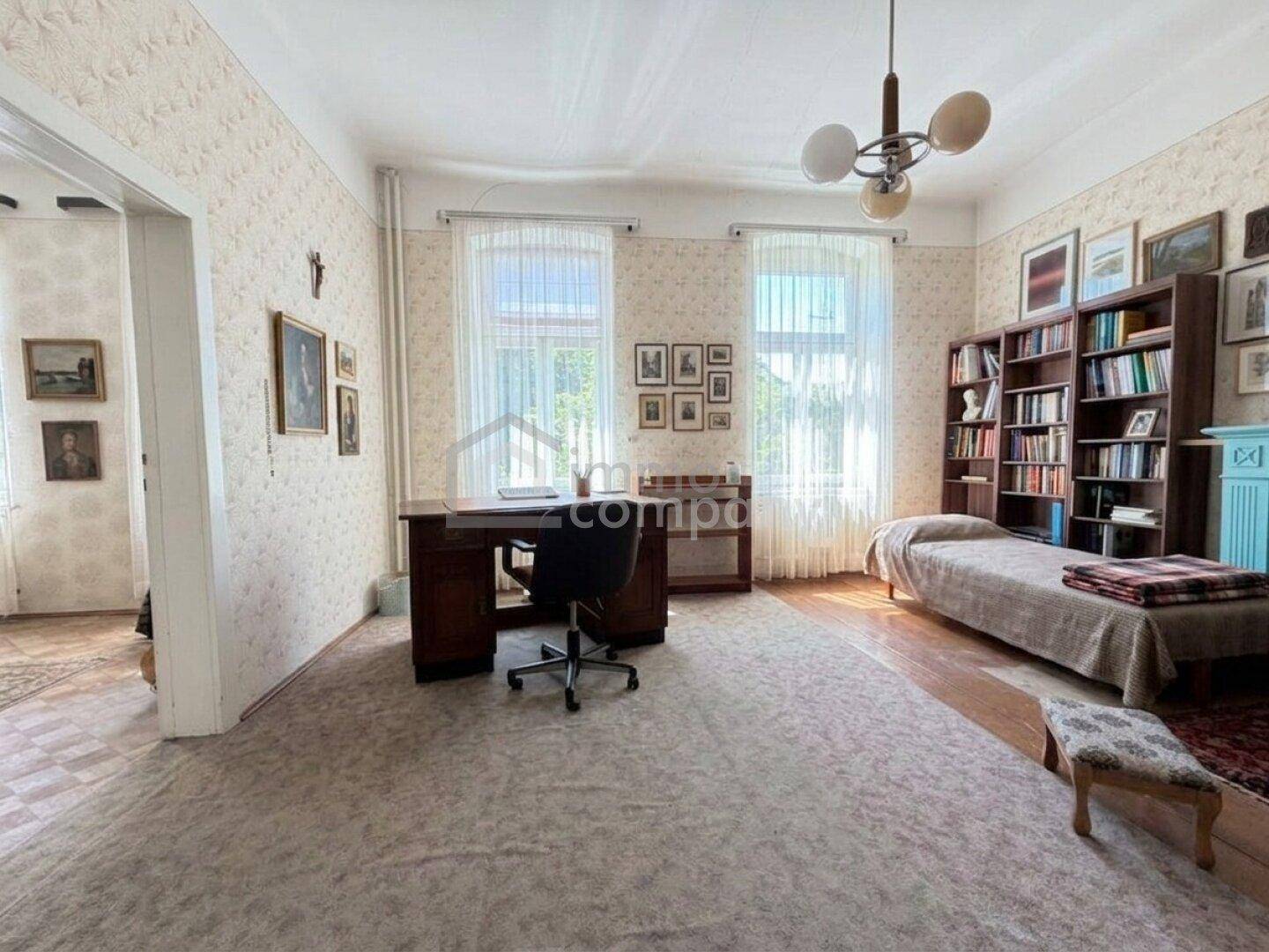 Geräumiges Arbeitszimmer mit Schreibtisch, Bücherregal und einem Einzelbett, ausgestattet mit Teppichboden und Tapete.